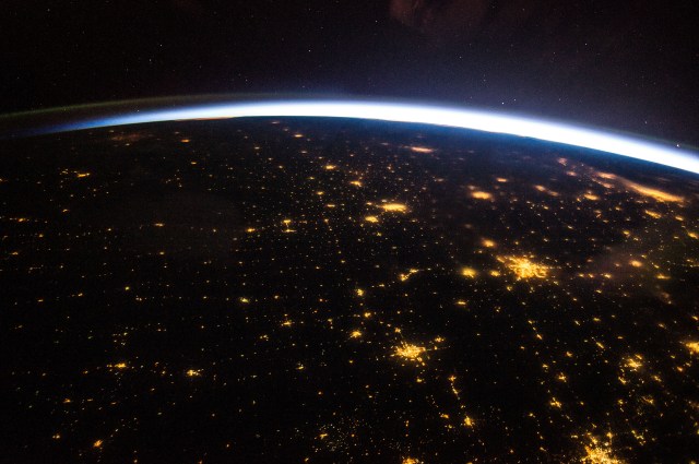 A dark Earth and sky with speckles of city lights visible