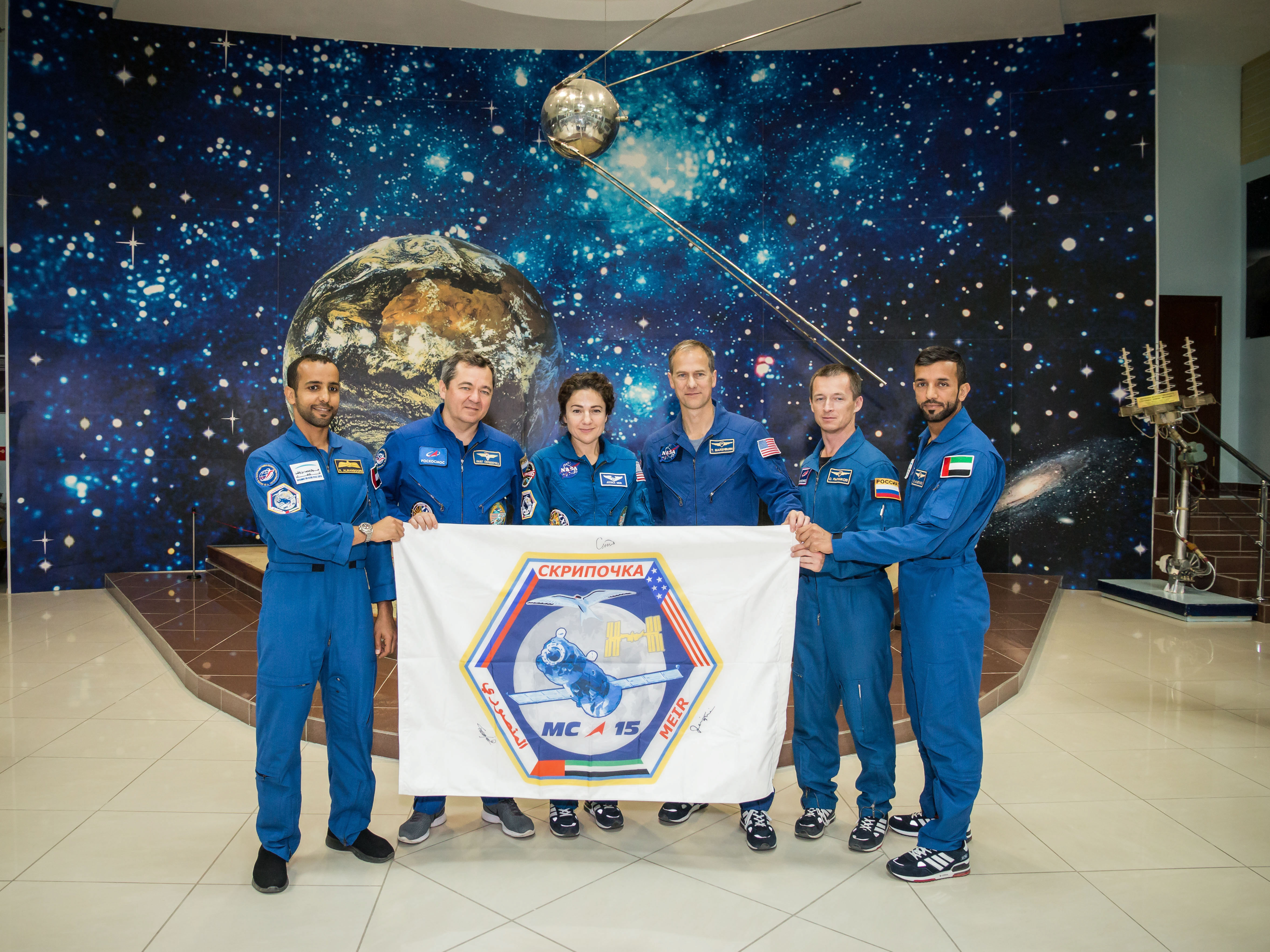At the Baikonur Cosmodrome Museum in Kazakhstan, the prime and backup crewmembers for the next launch to the International Space Station display a flag bearing the insignia of their Soyuz mission Sept. 20 during pre-launch activities. From left to right are the prime crew, spaceflight participant Hazzaa ali Almansoori of the United Arab Emirates and Expedition 61 crewmembers Oleg Skripochka of Roscosmos and Jessica Meir of NASA and backup crewmembers Tom Marshburn of NASA, Sergey Ryzhikov of Roscosmos and Sultan Al-Neyadi of the United Arab Emirates. Meir, Skripochka and Almansoori will launch Sept. 25 on the Soyuz MS-15 spacecraft for a mission on the International Space Station. Credit: NASA/Victor Zelentsov