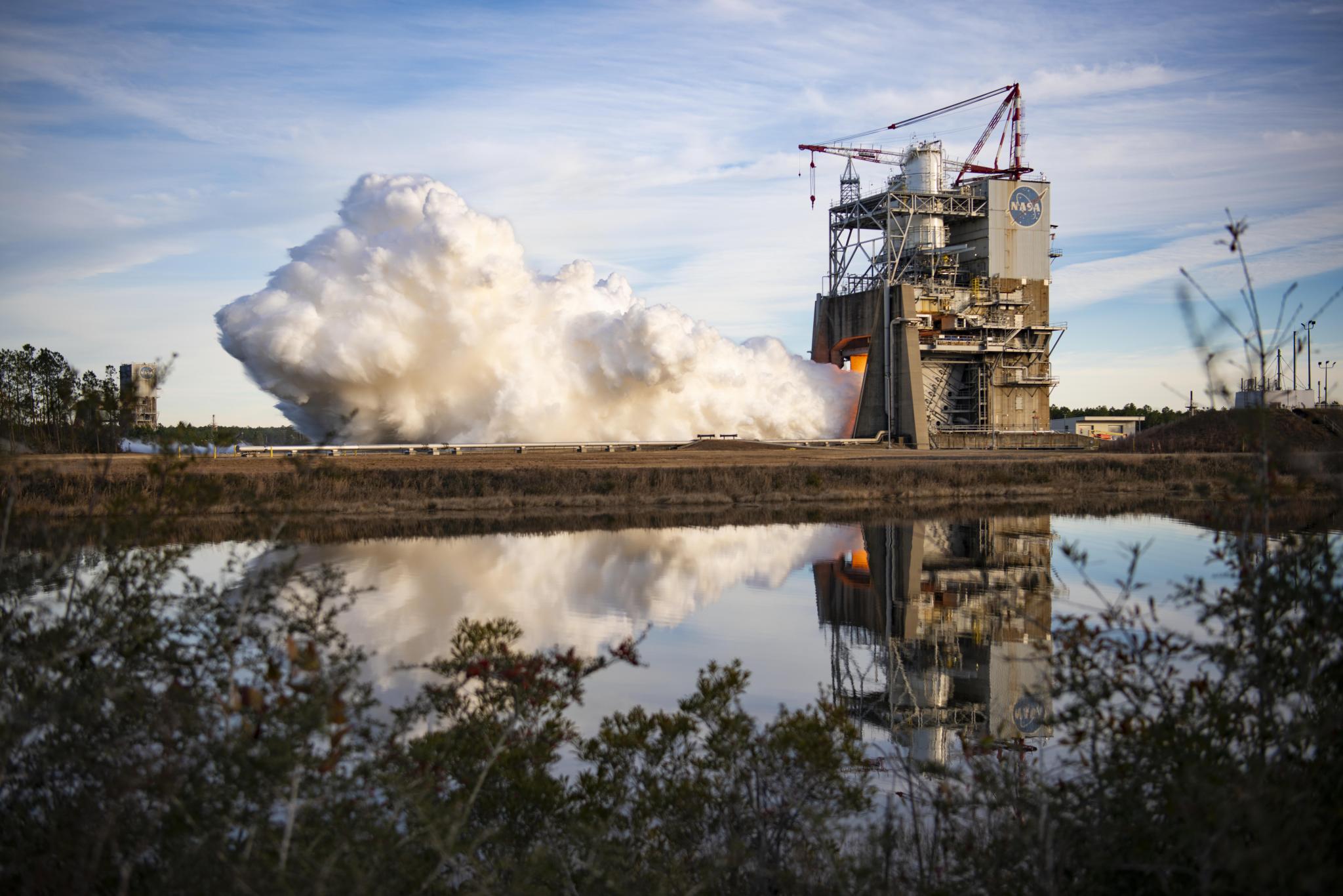 a hot fire of an RS-25 engine reflected in nearby body of water