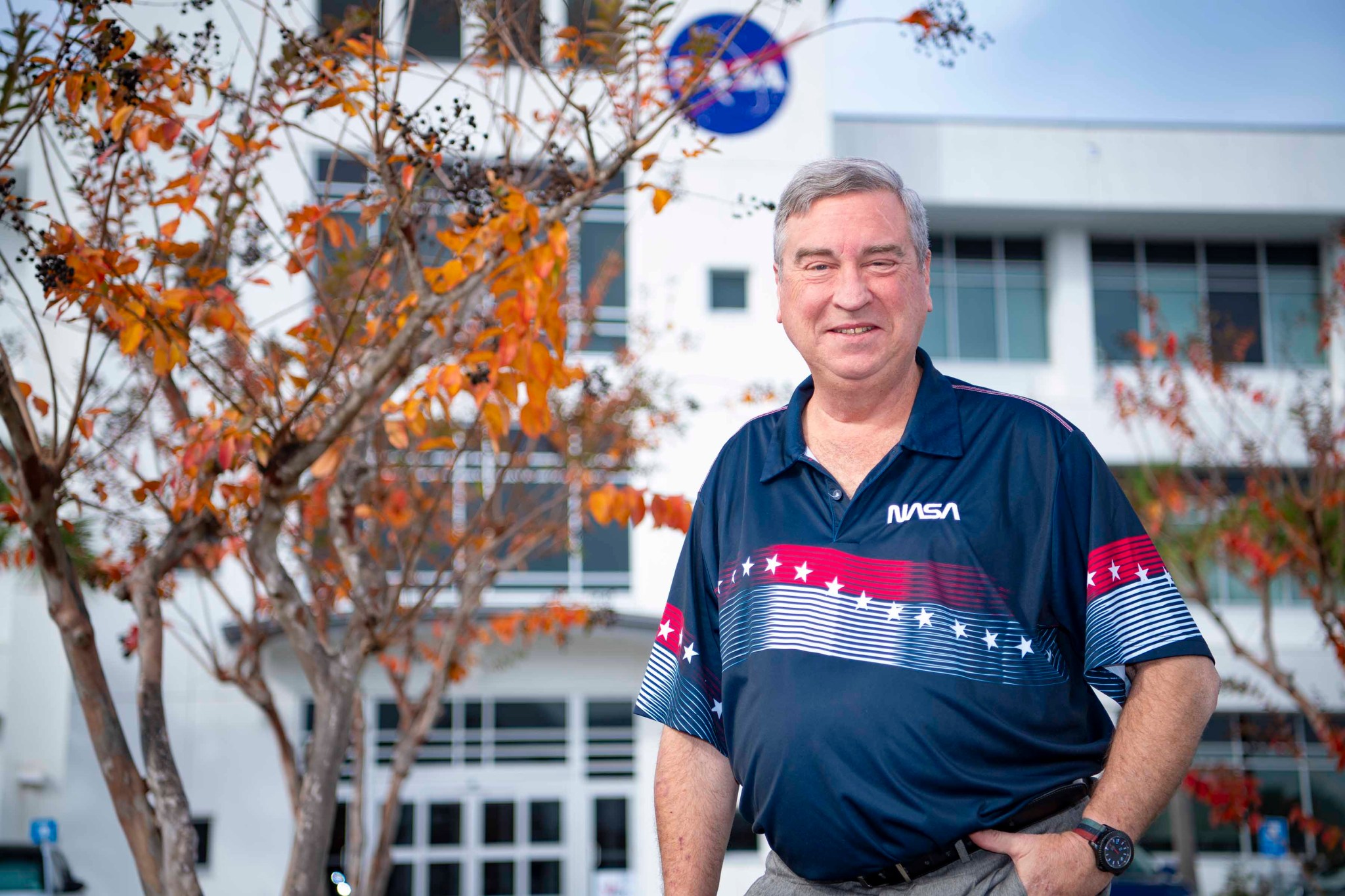 Tony Goretski, wearing a navy NASA polo shirt, smiles at the camera while standing outside of a building at NASA's Stennis Space Center