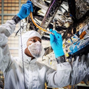 Male researcher in a white coverall with blue gloves working on a piece of hardware in a lab setting