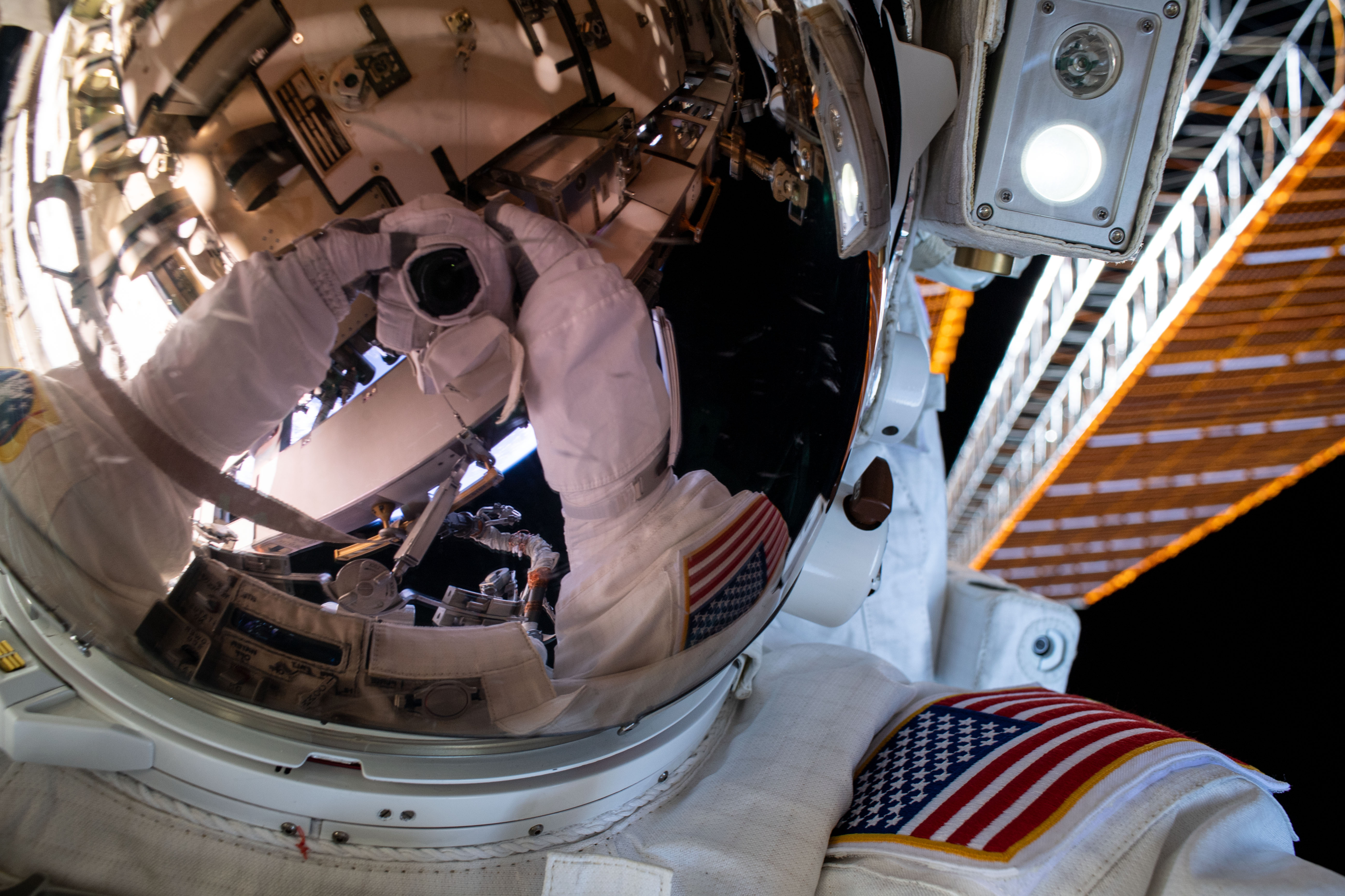 A spacewalker's spacesuit gloves and camera are reflected in the helmet visor in this "space-selfie" taken during a six-hour and seven-minute spacewalk.