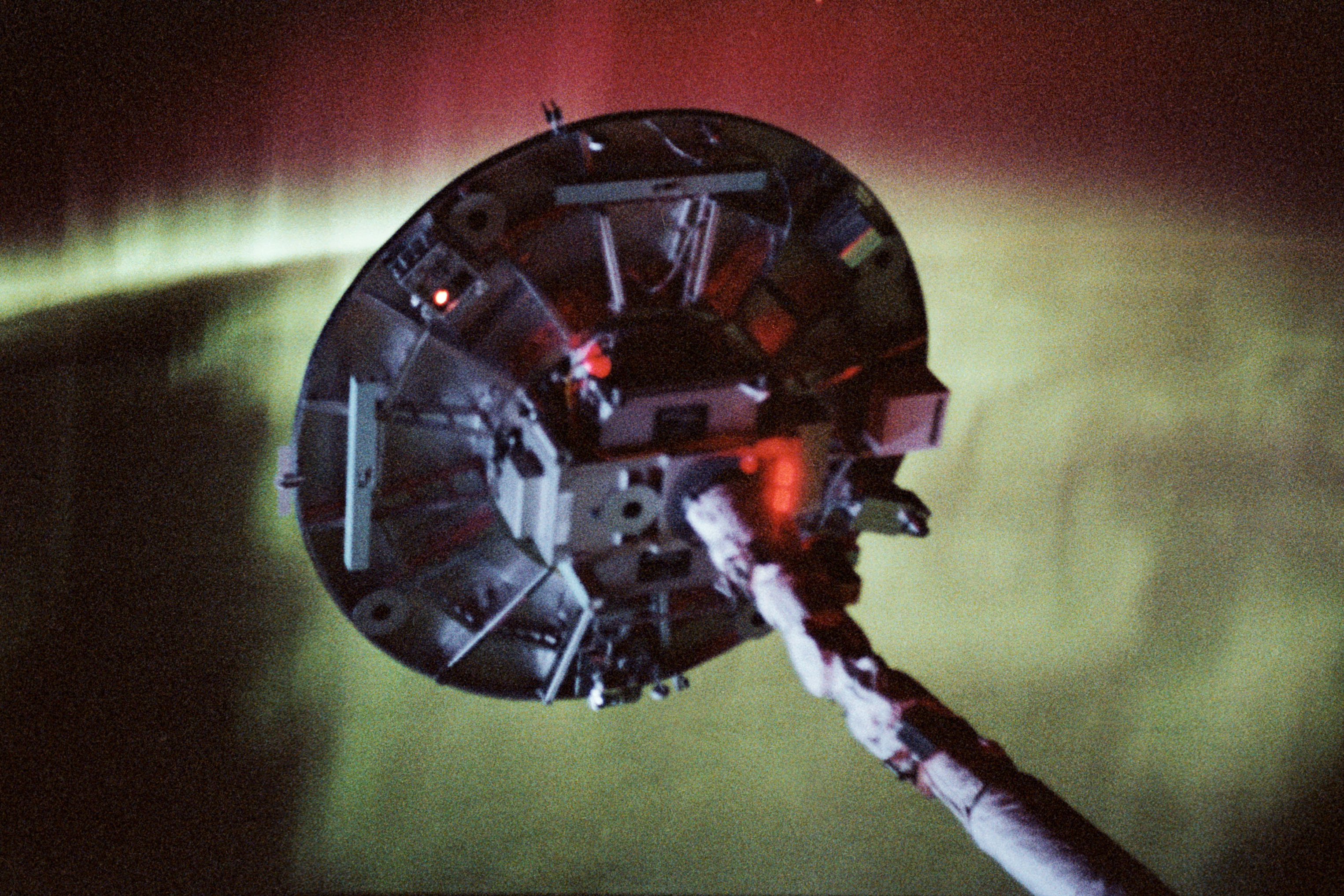 The Wake Shield Facility (WSF) deployed at the end of the Canadian-built Remote Manipulator System, with the aurora in the background