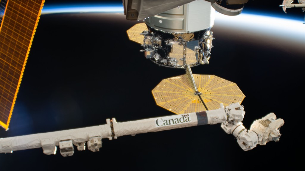 The Canadarm2 robotic arm is extended near the Northrop Grumman Cygnus resupply ship with its prominent cymbal-shaped UltraFlex solar arrays. The International Space Station was soaring above the South Pacific Ocean and into an orbital sunset at the time this photograph was taken.