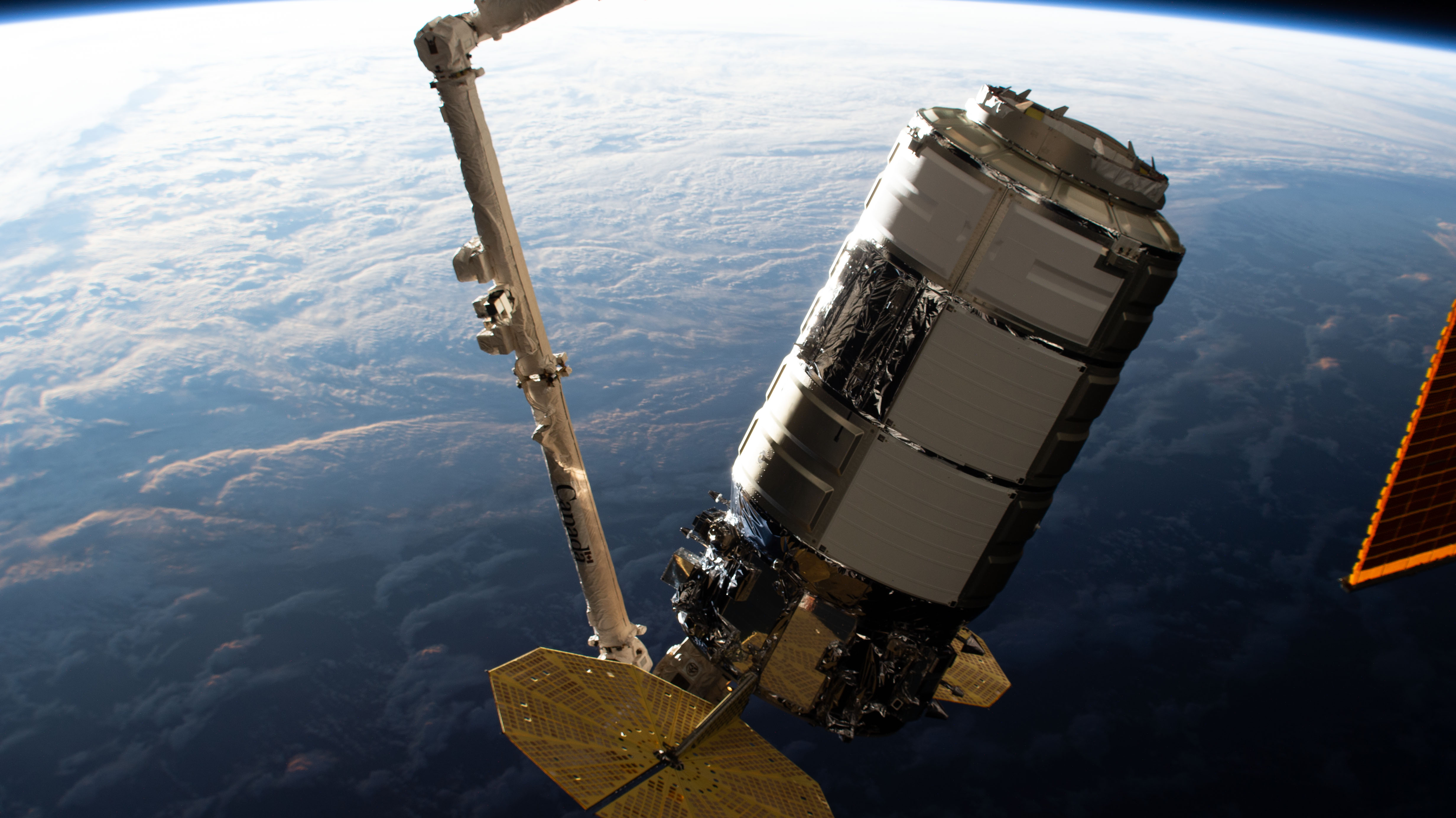 The Northrop Grumman Cygnus space freighter is pictured in the grips of the Canadarm2 robotic arm as mission controllers remotely guide the cargo vehicle to its installation point on the International Space Station's Unity module.