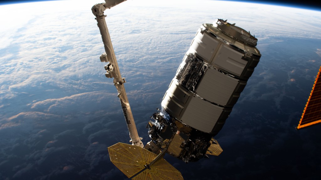 The Northrop Grumman Cygnus space freighter is pictured in the grips of the Canadarm2 robotic arm as mission controllers remotely guide the cargo vehicle to its installation point on the International Space Station's Unity module.