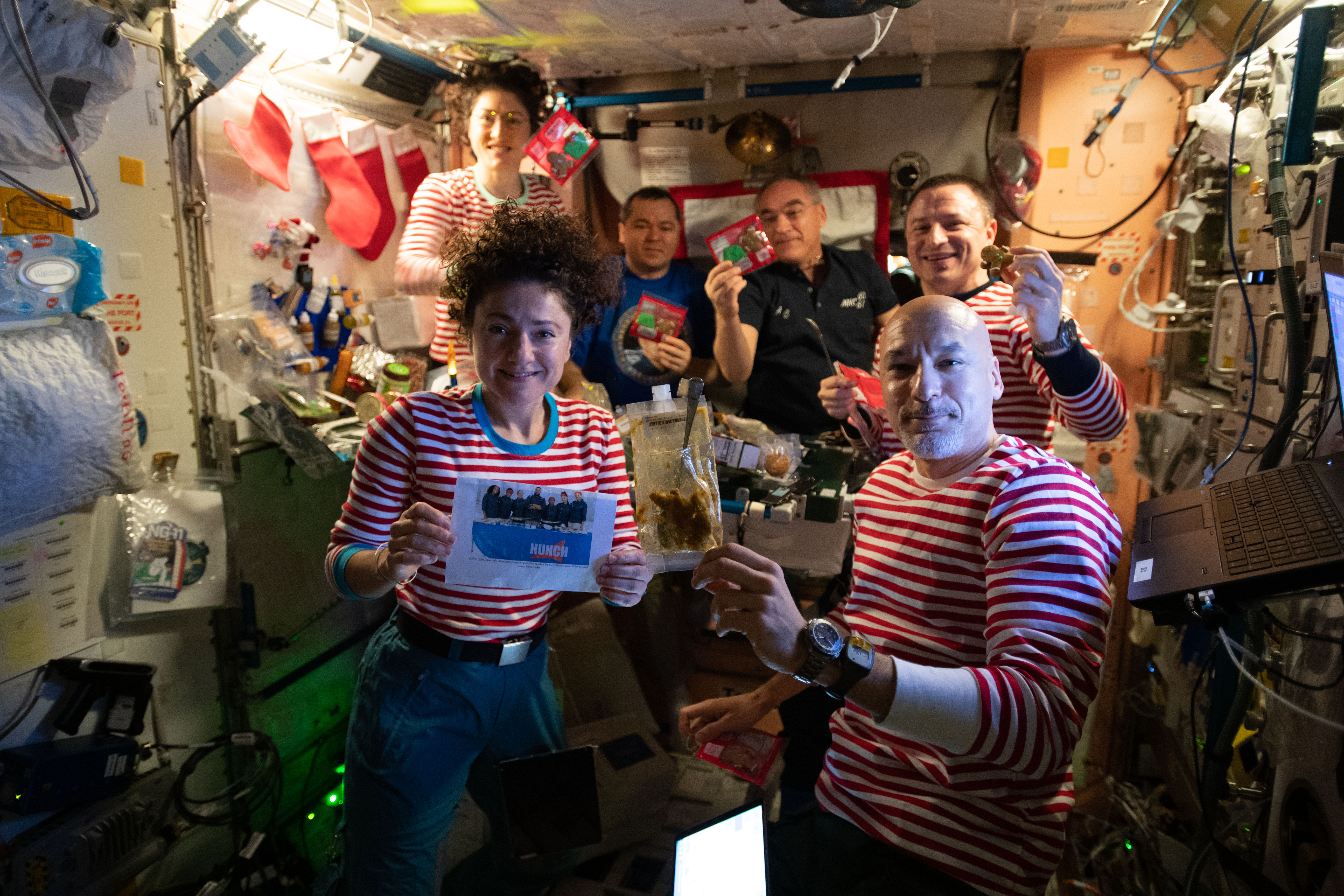 The Expedition 61 crew celebrates Christmas day with a brunch inside the International Space Station's Unity module decorated with stockings, flashlight "candles" and a Christmas tree banner. Clockwise from bottom left are, NASA Flight Engineers Jessica Meir and Christina Koch, Roscosmos Flight Engineers Oleg Skripochka and Alexander Skvortsov, NASA Flight Engineer Drew Morgan, and Commander Luca Parmitano of the European Space Agency (ESA).
