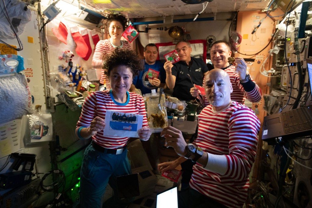 The Expedition 61 crew celebrates Christmas day with a brunch inside the International Space Station's Unity module decorated with stockings, flashlight "candles" and a Christmas tree banner. Clockwise from bottom left are, NASA Flight Engineers Jessica Meir and Christina Koch, Roscosmos Flight Engineers Oleg Skripochka and Alexander Skvortsov, NASA Flight Engineer Drew Morgan, and Commander Luca Parmitano of the European Space Agency (ESA).