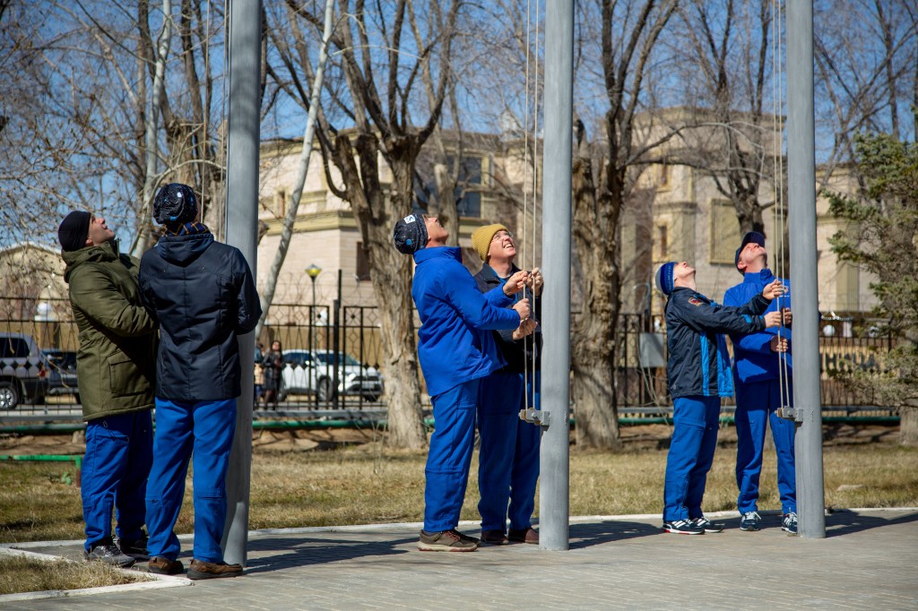 At the Cosmonaut Hotel crew quarters in Baikonur, Kazakhstan, the Expedition 63 prime and backup crewmembers raise the Russian, U.S. and Kazakh flags March 26 in a traditional ceremony. From left to right are prime crewmembers Ivan Vagner and Anatoly Ivanishin of Roscosmos, prime crewmember Chris Cassidy of NASA and his backup, Steve Bowen of NASA and backup crewmembers Sergey Ryzhikov and Andrei Babkin. Cassidy, Ivanishin and Vagner will launch April 9 from the Baikonur Cosmodrome on the Soyuz MS-16 spacecraft for a six-and-a-half month mission on the International Space Station. Credit: Courtesy/Roscosmos.