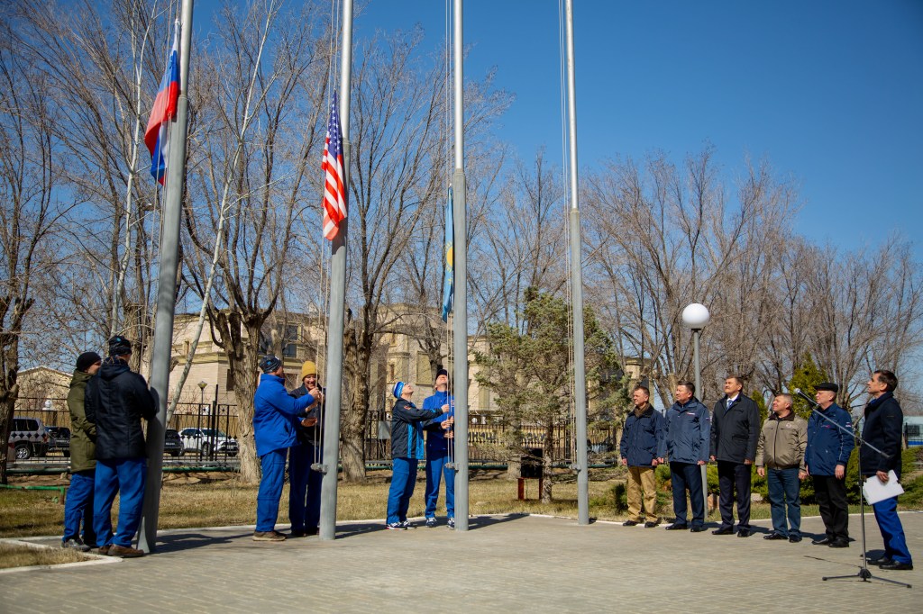 At the Cosmonaut Hotel crew quarters in Baikonur, Kazakhstan, the Expedition 63 prime and backup crewmembers raise the Russian, U.S. and Kazakh flags March 26 in a traditional ceremony. From left to right are prime crewmembers Ivan Vagner and Anatoly Ivanishin of Roscosmos, prime crewmember Chris Cassidy of NASA and his backup, Steve Bowen of NASA and backup crewmembers Sergey Ryzhikov and Andrei Babkin. Cassidy, Ivanishin and Vagner will launch April 9 from the Baikonur Cosmodrome on the Soyuz MS-16 spacecraft for a six-and-a-half month mission on the International Space Station. Credit: Courtesy/Roscosmos.