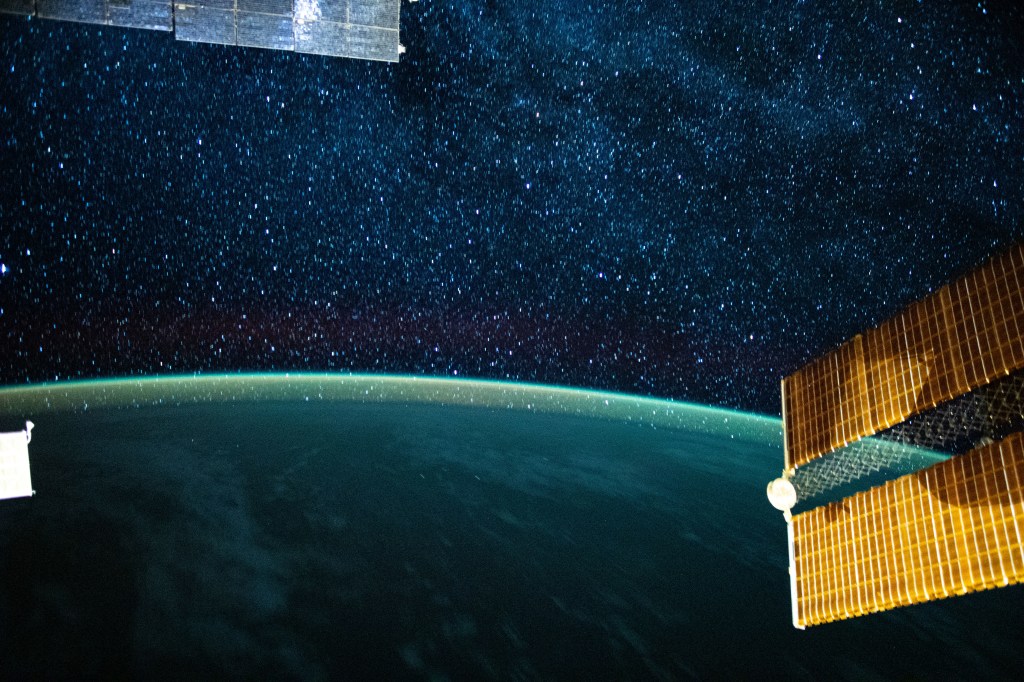 This long-exposure photograph from the International Space Station was taken during an orbital night period and reveals the Milky Way glittering above a bright but exaggerated atmospheric glow blanketing the Earth's horizon.