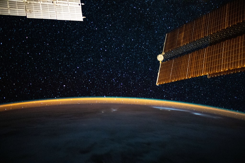 This long-exposure photograph from the International Space Station was taken during an orbital night period and reveals the Milky Way glittering above a bright but exaggerated atmospheric glow blanketing the Earth's horizon.