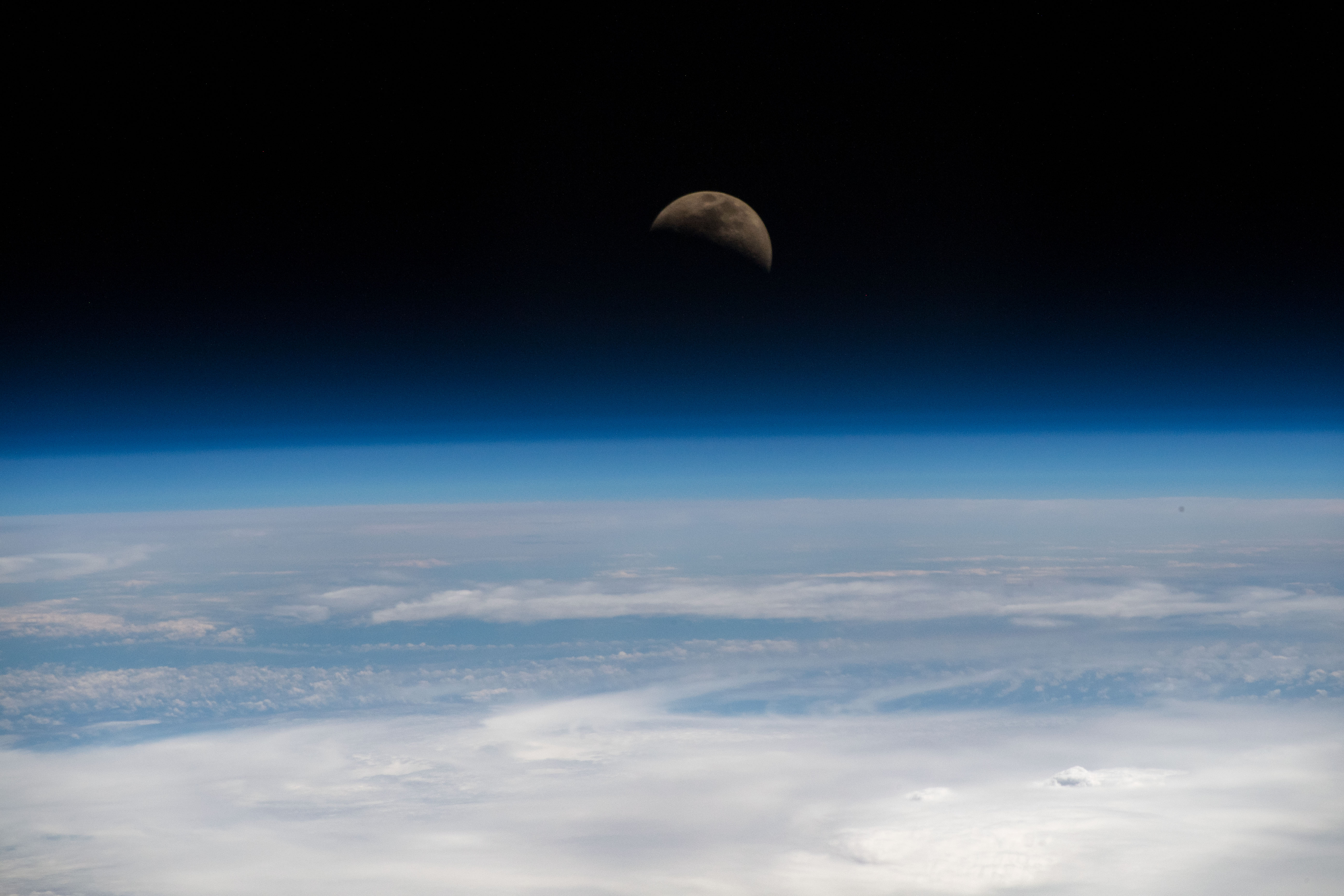 The moon is photographed in its first quarter phase just above the Earth's limb as the International Space Station orbited 255 miles above the Pacific Ocean south of the Hawaiian island chain.