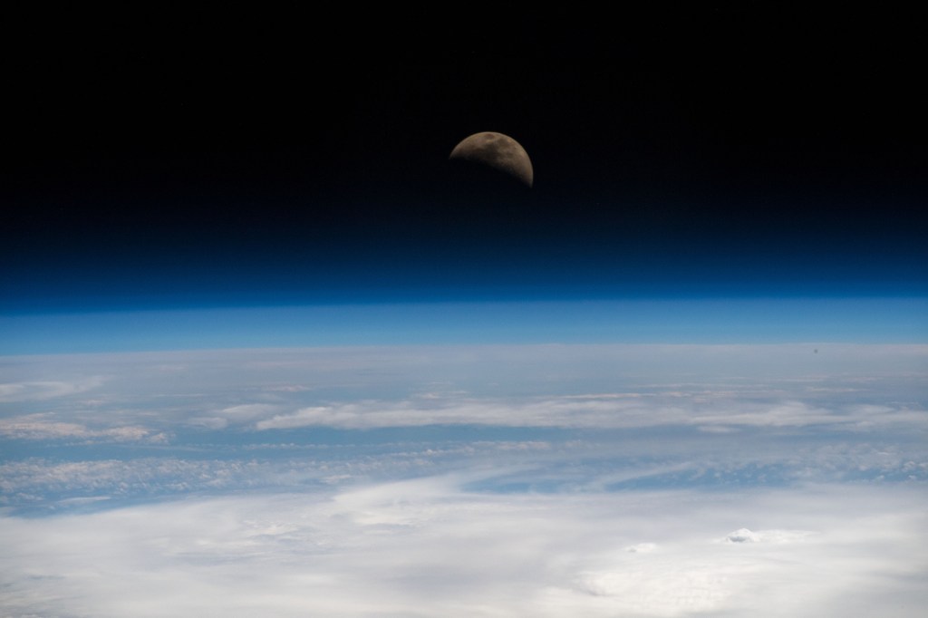 The moon is photographed in its first quarter phase just above the Earth's limb as the International Space Station orbited 255 miles above the Pacific Ocean south of the Hawaiian island chain.