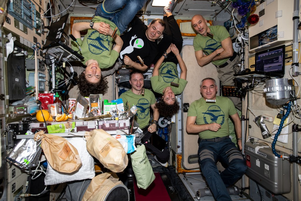 The six-member Expedition 61 crew is gathered together inside the Zvezda service module for a New Year's Eve meal. Clockwise from top left are, Flight Engineers Christina Koch of NASA and Oleg Skripochka of Roscosmos; Commander Luca Parmitano of ESA (European Space Agency); Flight Engineers Alexander Skvortsov of Roscosmos and Jessica Meir and Andrew Morgan, both from NASA.