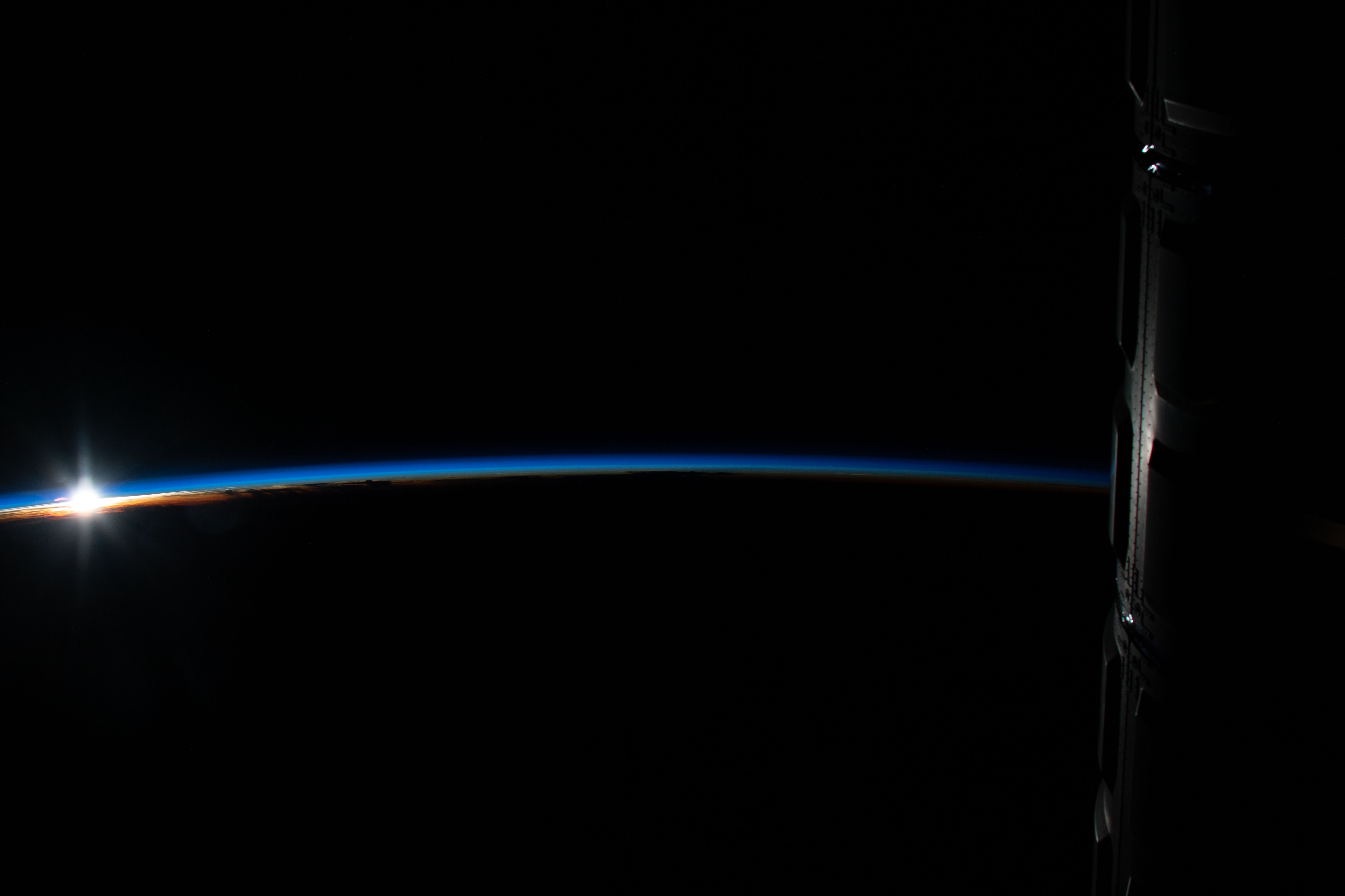 The sun's first rays peek above Earth's limb highlighting the thin blue atmosphere during an orbital sunrise as the International Space Station orbited 255 miles above Indonesia.