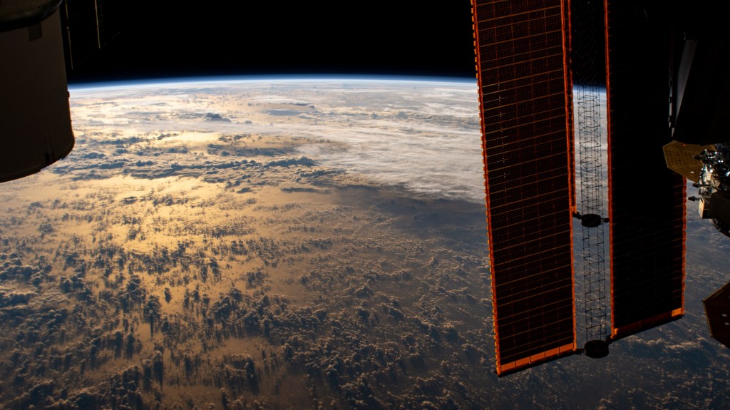 The International Space Station orbits 267 miles above the Earth as the Sun's glint beams over the Philippine Sea highlighting the clouds and their shadows during an orbital sunrise.