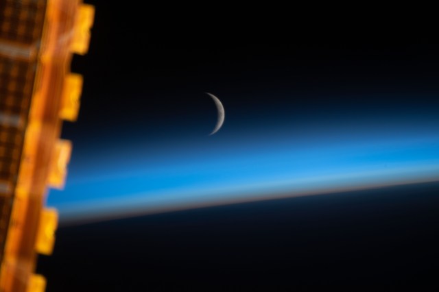 The waxing crescent moon is photographed just above Earth's limb and the bluish hue of the atmosphere at the beginning of an orbital sunrise. A portion of one of the International Space Station's solar arrays is seen in the left foreground as the orbital complex flew 258 miles above the Sea of Japan.