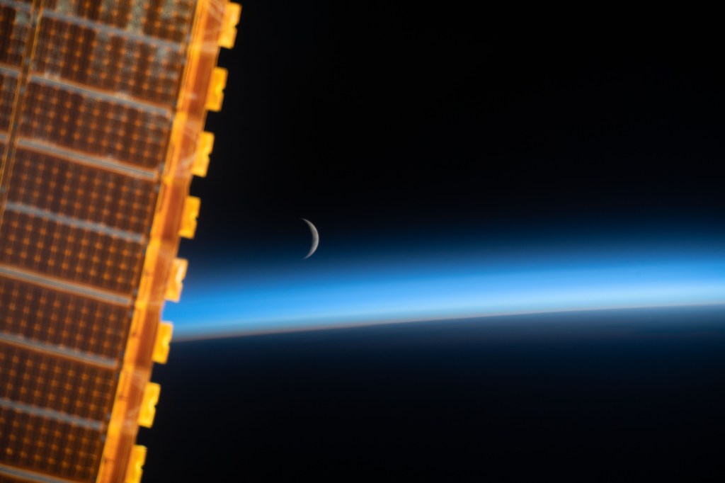 The waxing crescent moon is photographed just above Earth's limb and the bluish hue of the atmosphere at the beginning of an orbital sunrise. A portion of one of the International Space Station's solar arrays is seen in the left foreground as the orbital complex flew 258 miles above the Sea of Japan.
