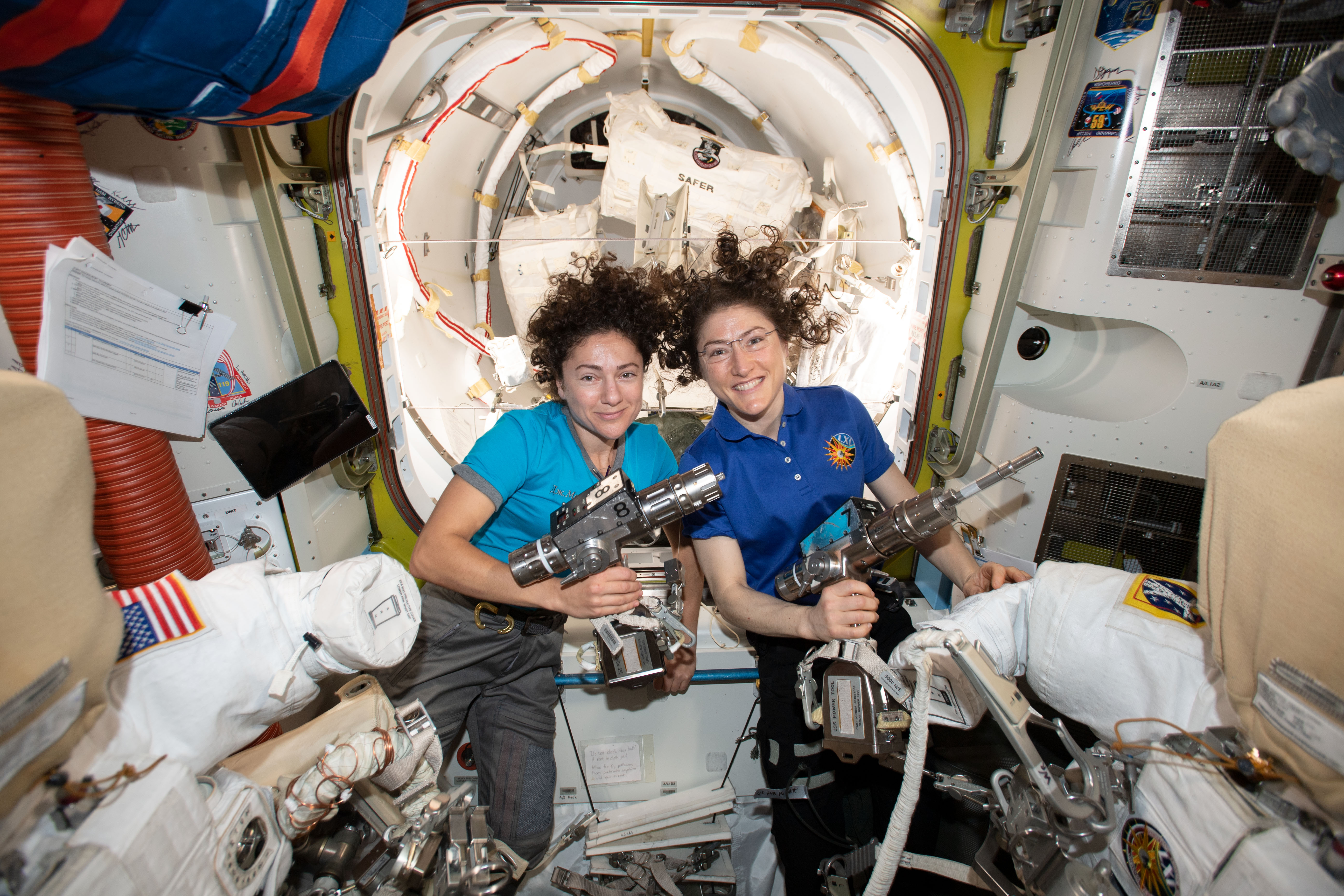 NASA astronauts Jessica Meir (left) and Christina Koch are inside the Quest airlock preparing the U.S. spacesuits and tools they will use on their first spacewalk together. The Expedition 61 flight engineers are holding the pistol grip tools they will use to swap out a failed power controller, also known as a battery charge-discharge unit, that regulates the charge to batteries that collect and distribute power to the International Space Station.