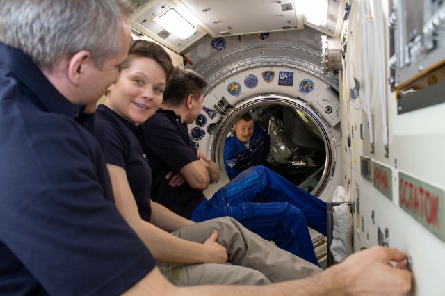 Waiting inside the Rassvet module to greet their new Expedition 59 crewmates are (foreground to back) Flight Engineers David Saint-Jacques and Anne McClain and Commander Oleg Kononenko. New Expedition 59 Flight Engineer Alexey Ovchinin peers into the International Space Station moments after opening the hatch to the Soyuz MS-12 spacecraft. NASA astronauts Nick Hague and Christina Koch (out of frame) would soon fly into the orbital lab for the first time.
