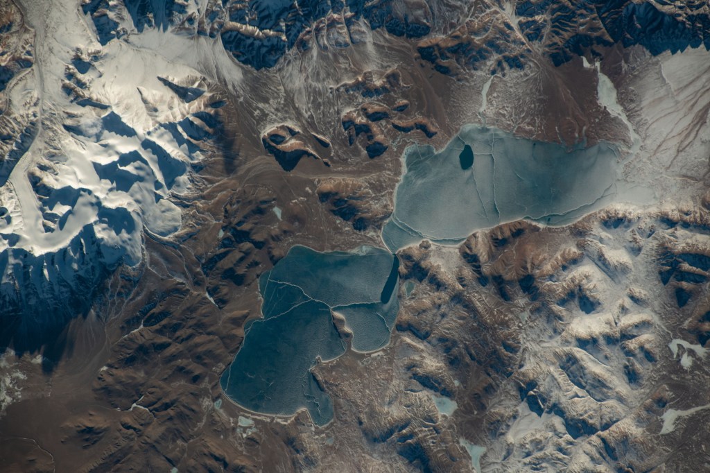 iss070e088503 (Feb. 8, 2024) -- A duo of Tibetan lakes, Qingche and Luotuo, are covered with ice as snow drifts through the mountainous terrain. The International Space Station was orbiting 260 miles above when NASA astronaut Jasmin Moghbeli captured this image.