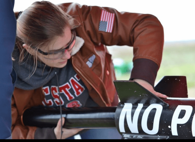 A college student works on a student created rocket with safety glasses on her face.