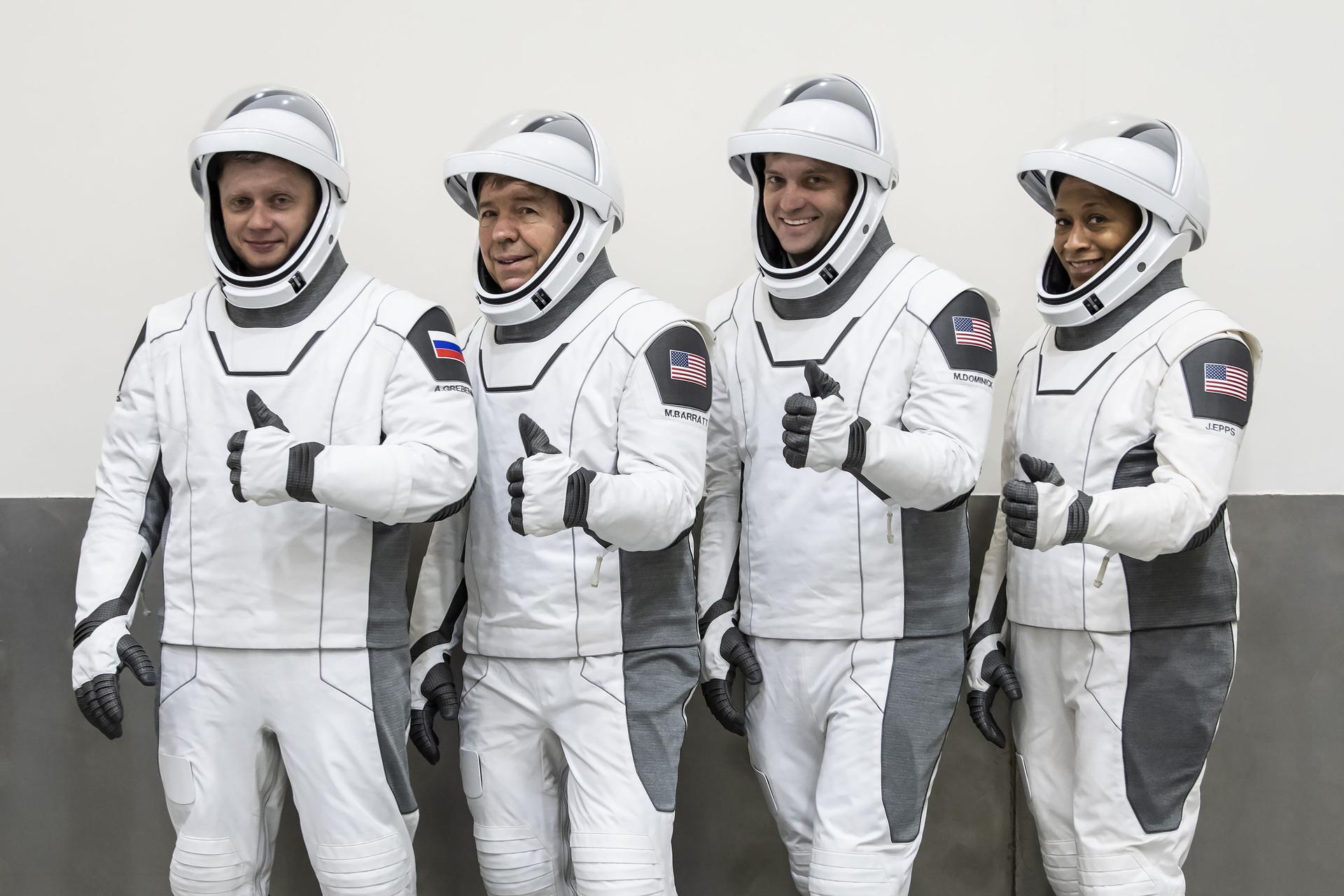 One Russian cosmonaust and three astronauts, three men and one woman, stand next to each other to pose for a photo.