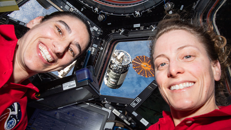 Astronauts (from left) Jasmin Moghbeli and Loral O'Hara are pictured inside the cupola with the Cygnus resupply ship outside in the grips of the Canadarm2 robotic arm.