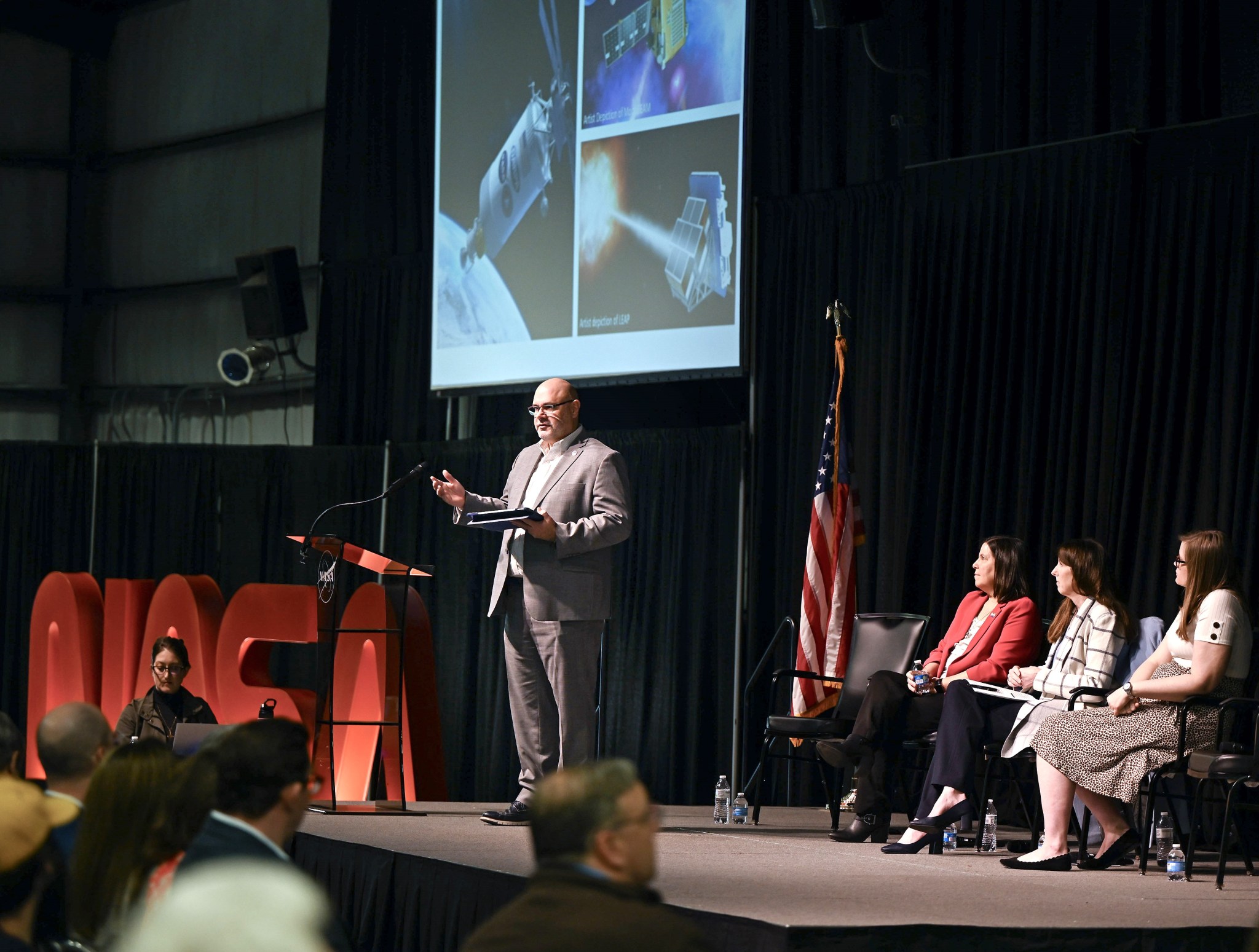 NASA Marshall Space Flight Center Director Joseph Pelfrey, standing, discusses the direction of Marshall and the center's upcoming projects and strategies during the first all-hands meeting of 2024. Joining him on stage, from left, are Tia Ferguson, Marshall's Space Systems Department director in the Engineering Directorate, Associate Center Director Rae Ann Meyer, and Mallory James, an aerospace engineer and management assistant in the office of the center director.