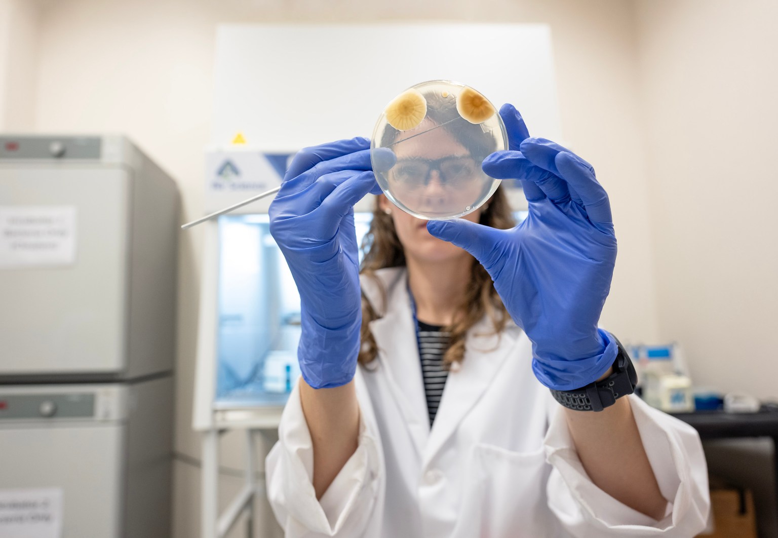 Marshall Space Flight Center's Chelsi Cassilly holds a Petri dish in front of her toward the camera and examines the specimen collected.