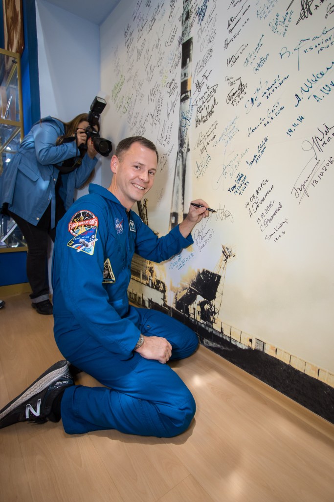 At the Baikonur Cosmodrome Museum in Kazakhstan, Expedition 57 crewmember Nick Hague of NASA signs a mural Oct. 6 as part of traditional pre-launch activities. Hague and Alexey Ovchinin of Roscosmos will launch Oct. 11 from the Baikonur Cosmodrome on the Soyuz MS-10 spacecraft for a six-month mission on the International Space Station.