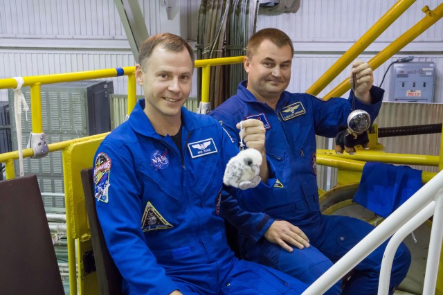 At the Baikonur Cosmodrome in Kazakhstan, Expedition 57 crew members Nick Hague of NASA (left) and Alexey Ovchinin of Roscosmos (right) hold up toy mascots Oct. 6 during final fit check activities prior to launch. The mascots will be mounted over their heads in the Soyuz MS-10 spacecraft to serve as “zero-G” indicators when they launch Oct. 11 for a six-month mission on the International Space Station.
