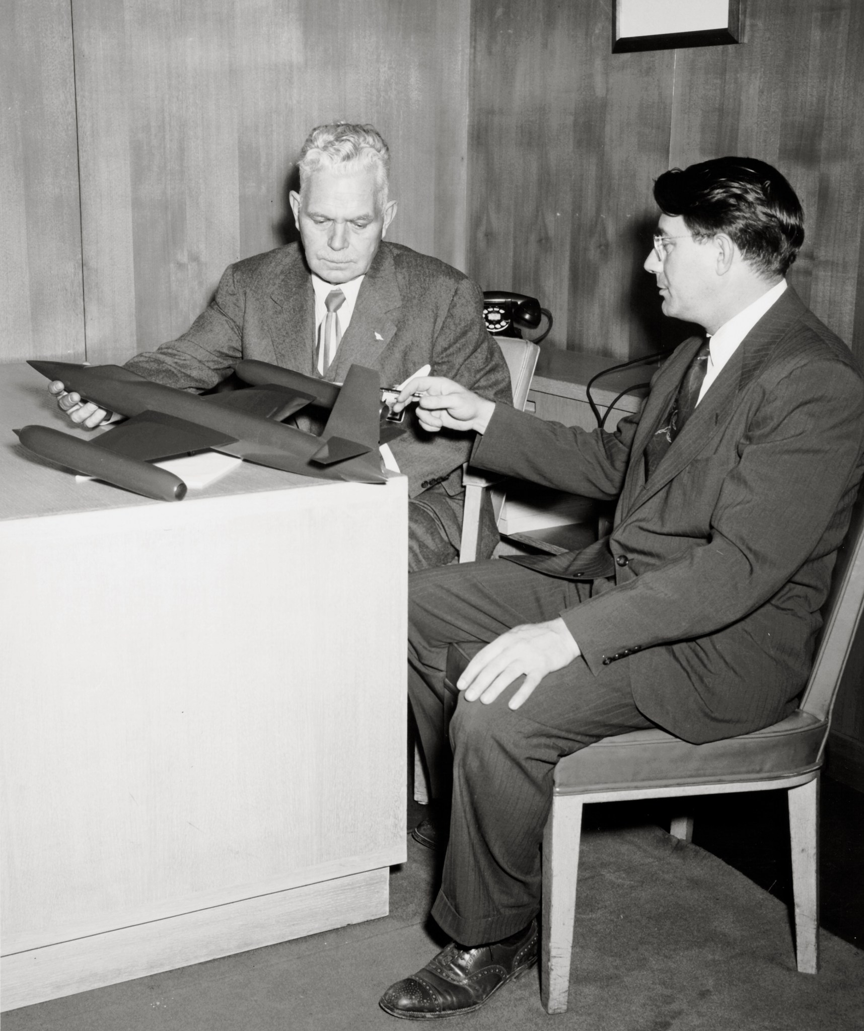 Two men at desk with aircraft model.