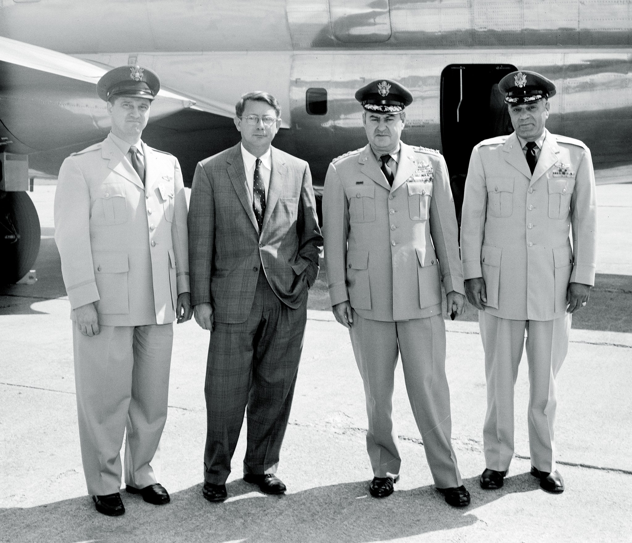 Three military officers standing with man on tarmac.