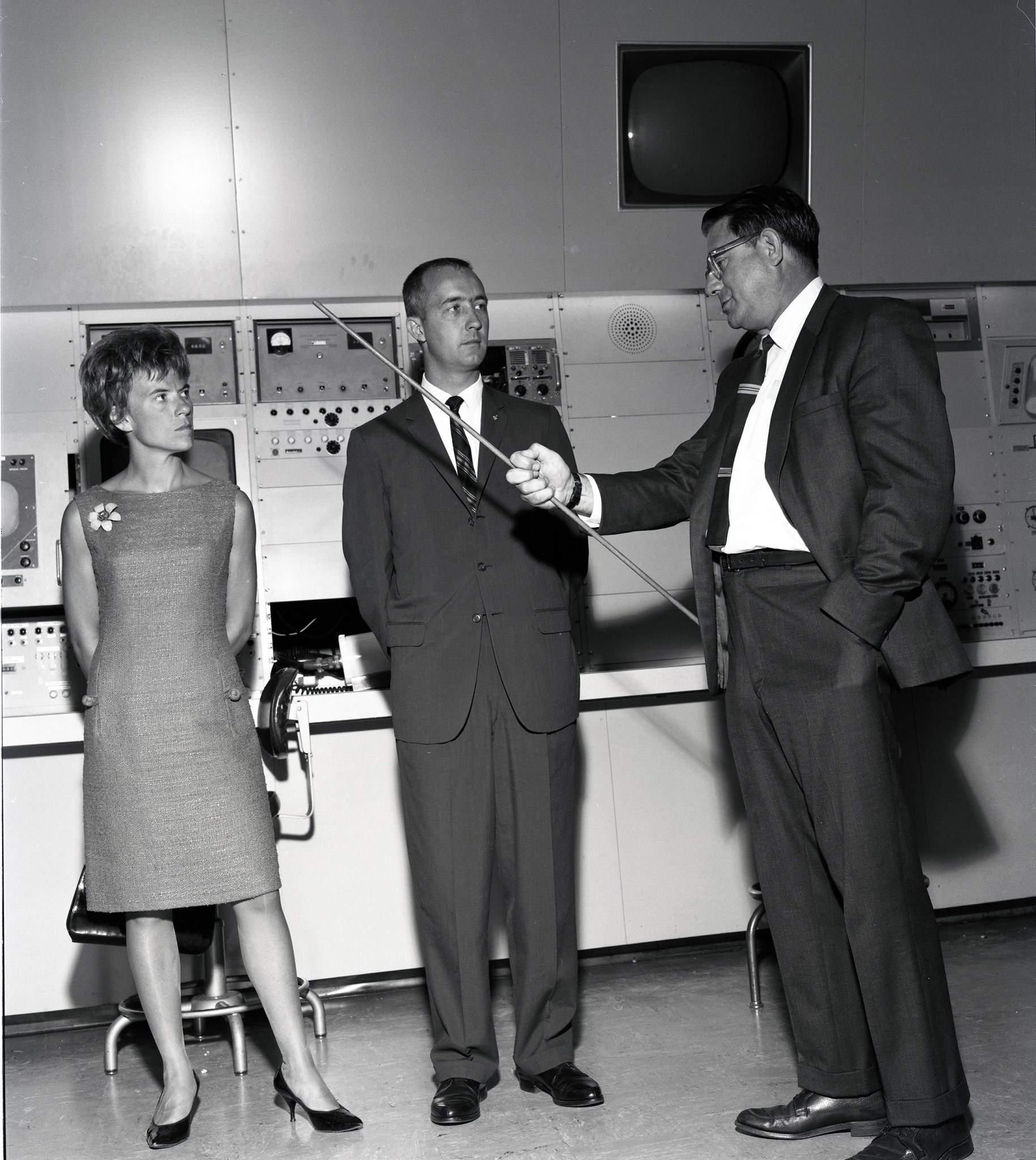 Man with pointer talks to couple in control room.