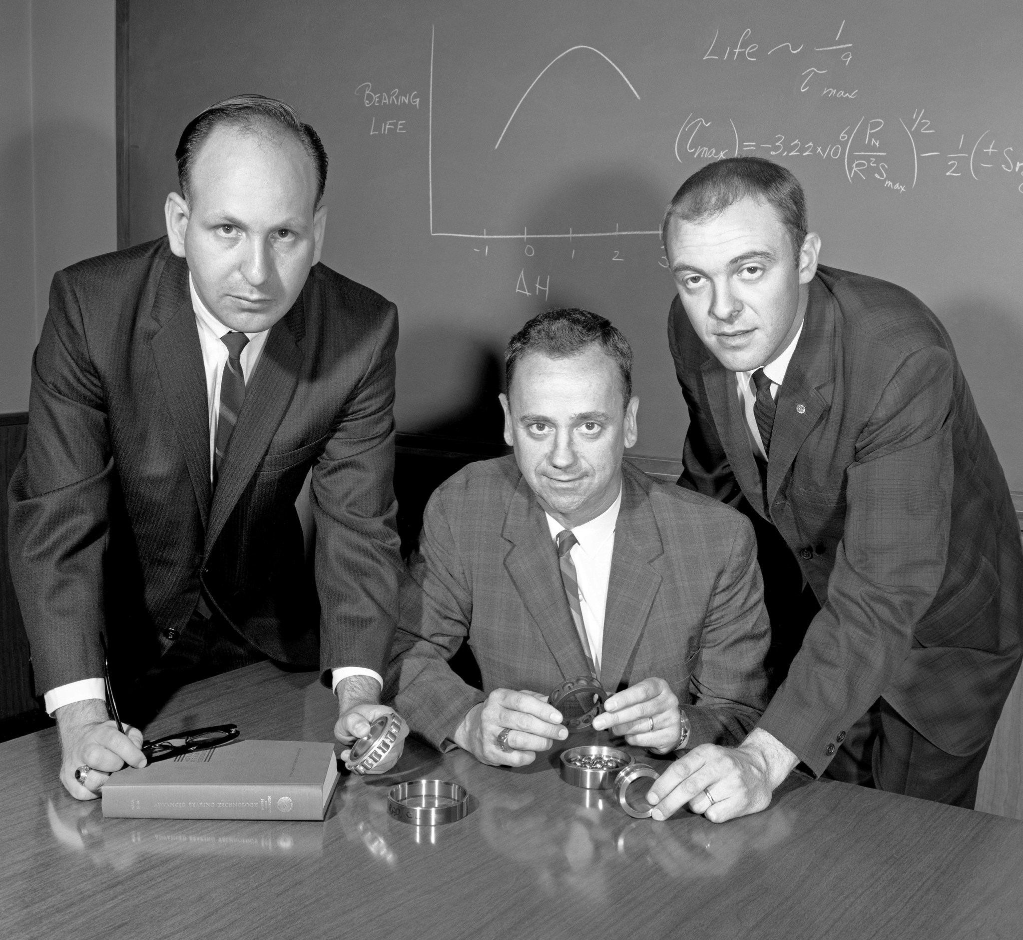 Three men hunched over table.