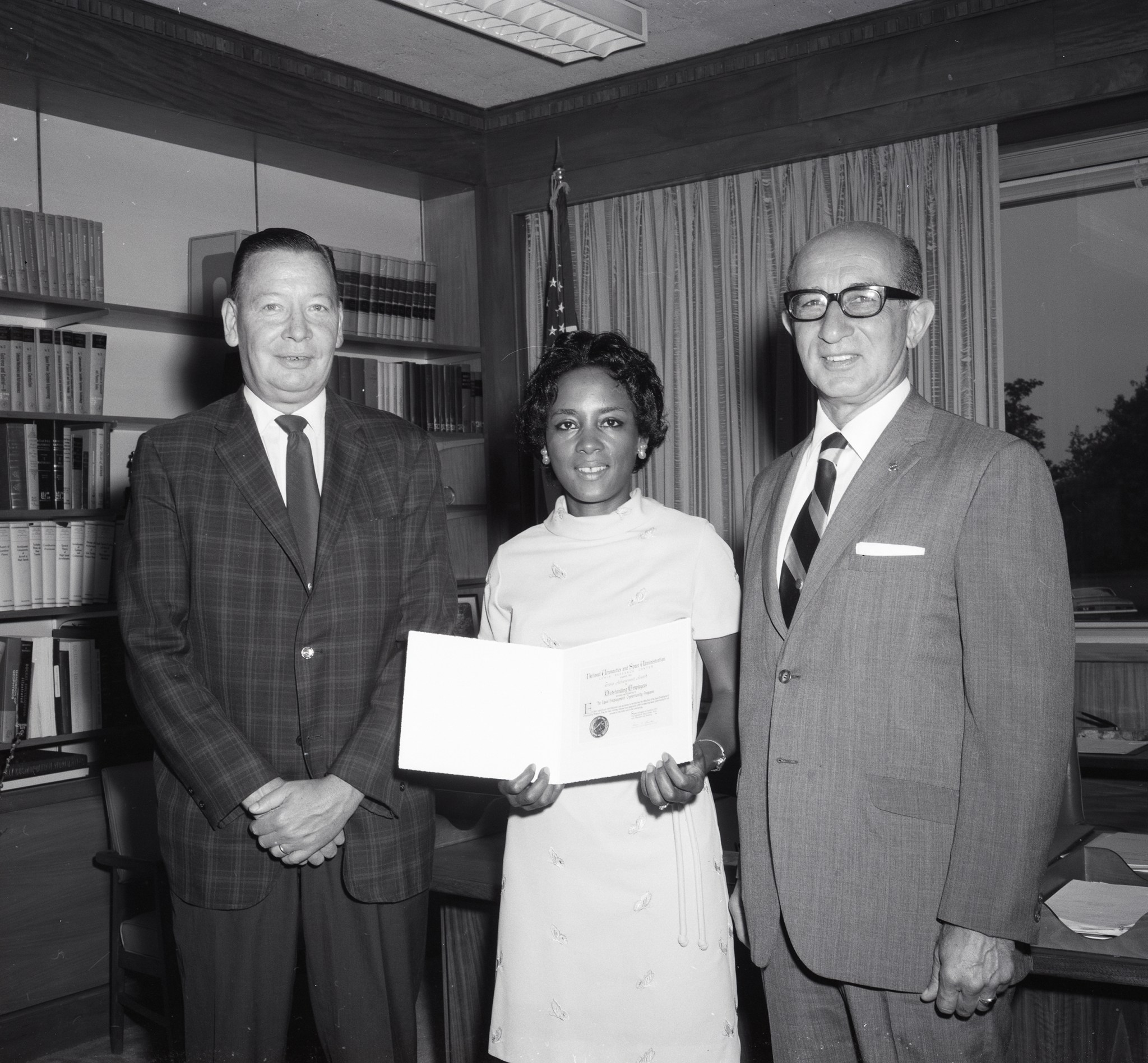 Woman holding award, standing between two men.
