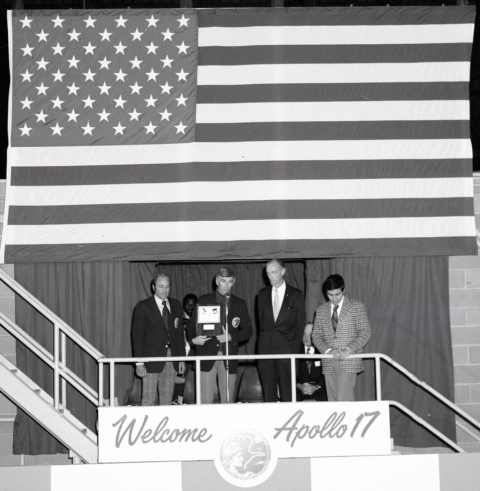 Four men standing in front of flag.