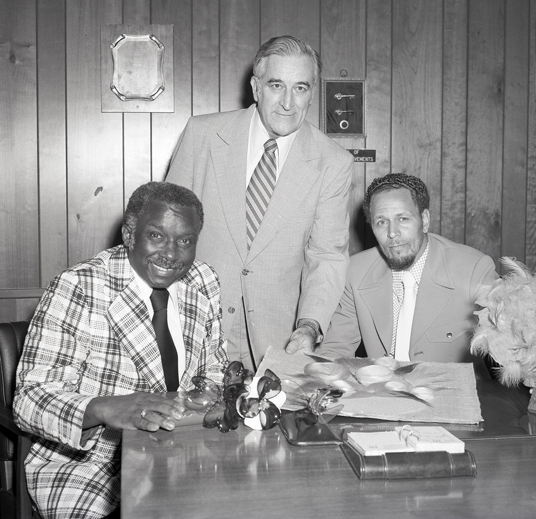 Two seated men with another standing between.