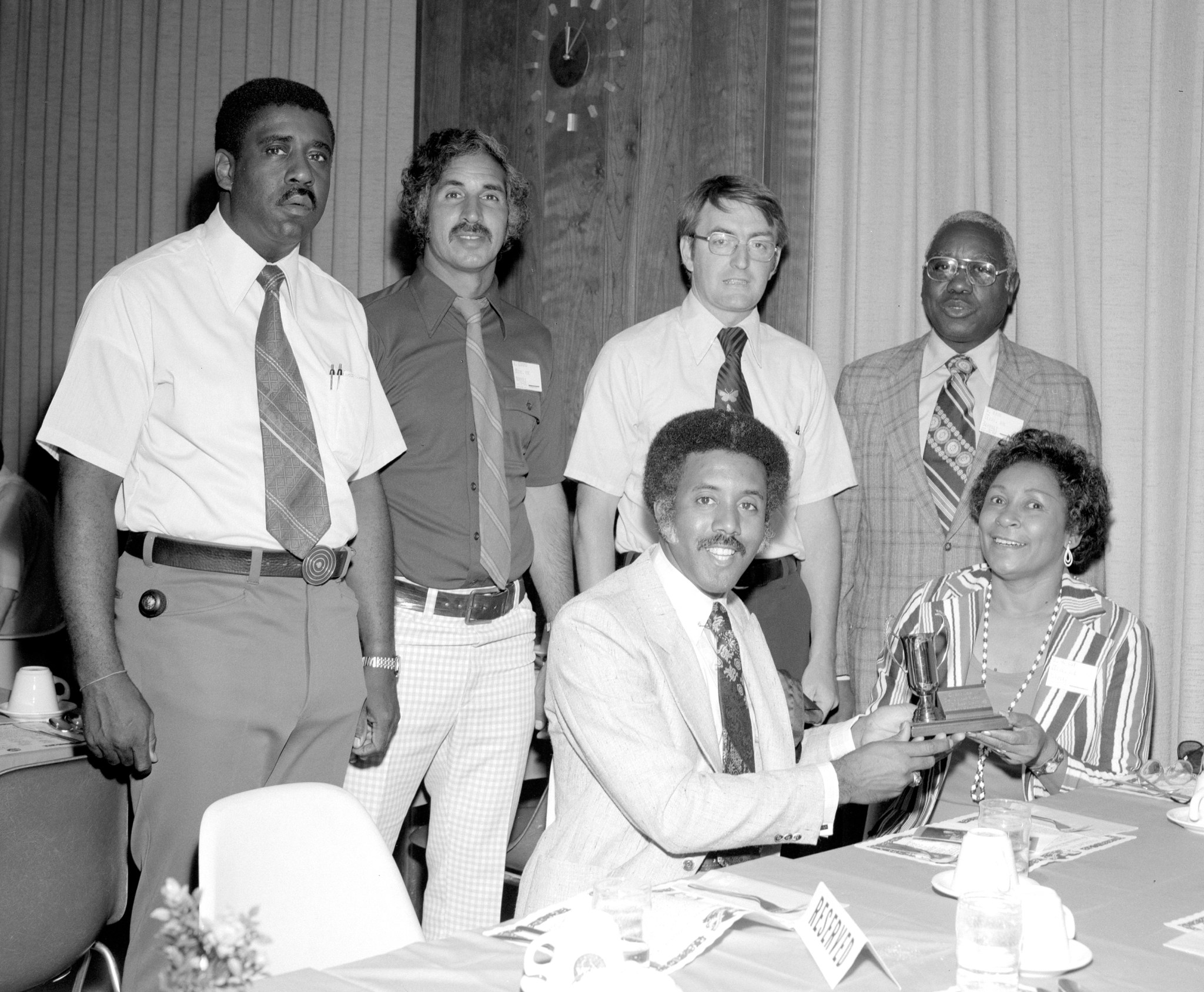 Man and woman holding trophy with several men standing behind.