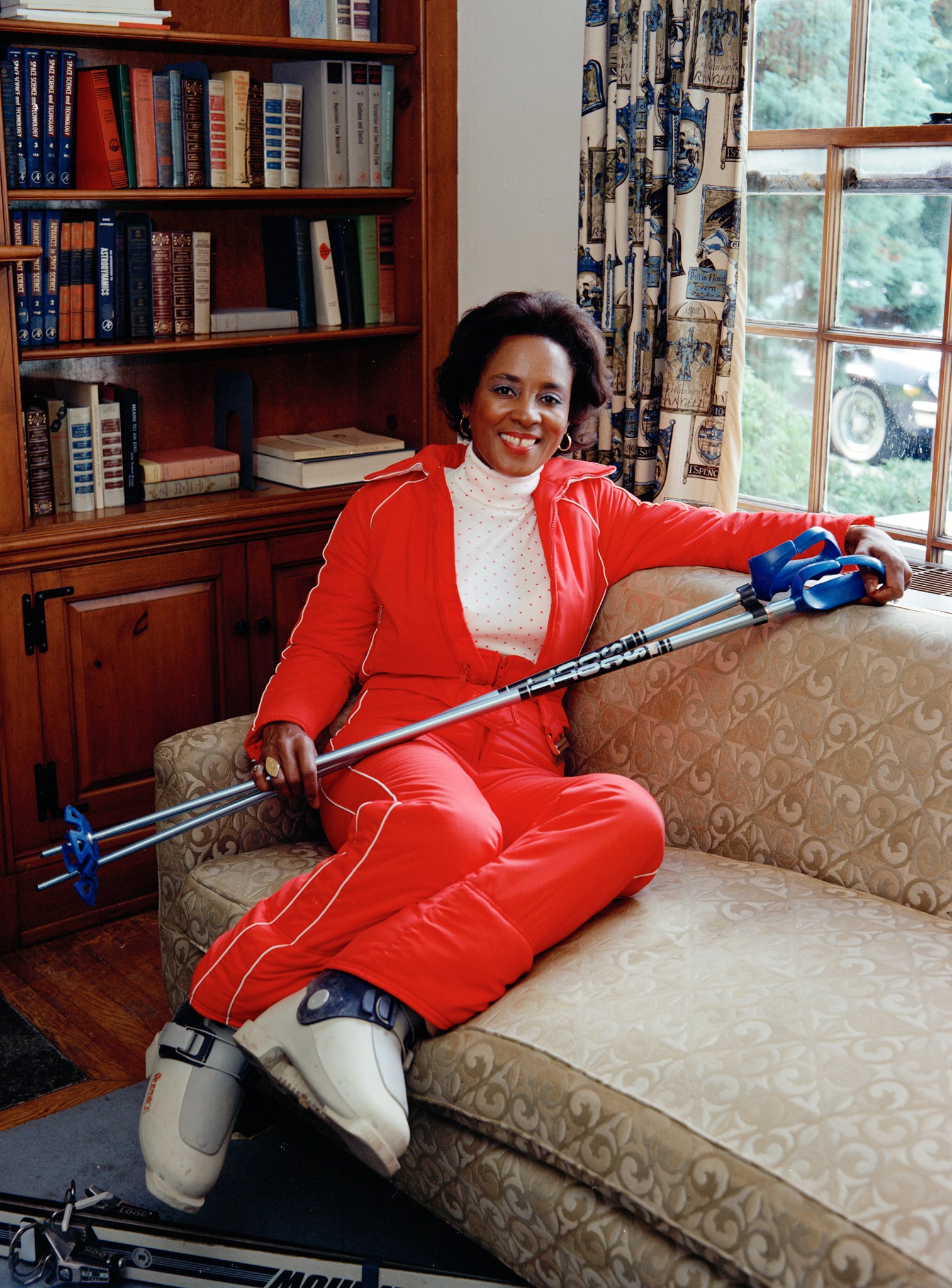 Woman seated indoors in ski outfit.