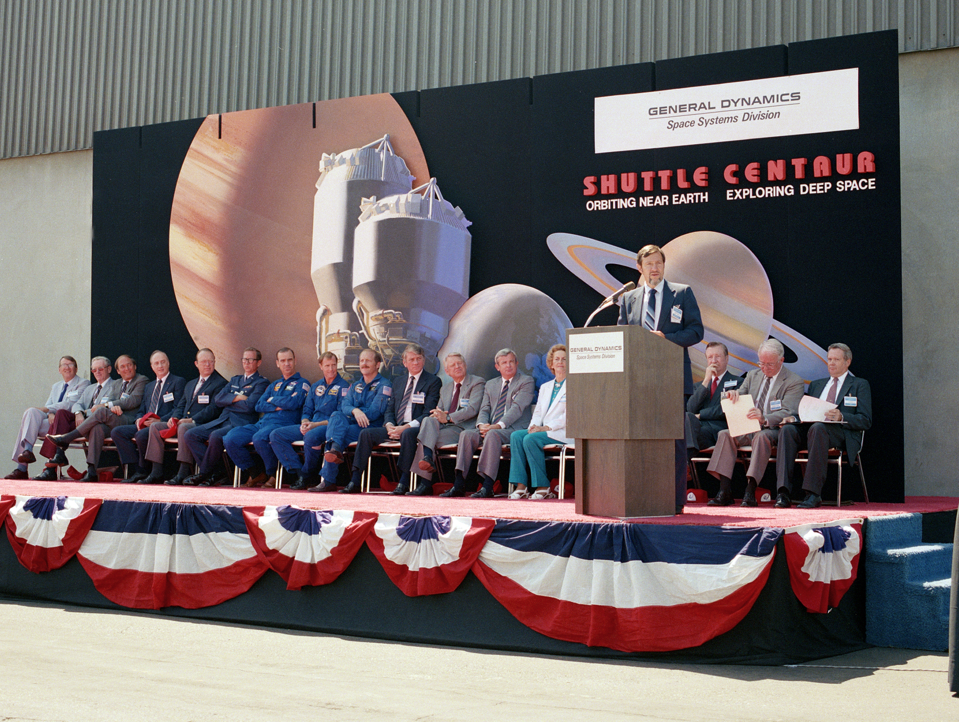 Speaker and seated guests on outdoor stage.