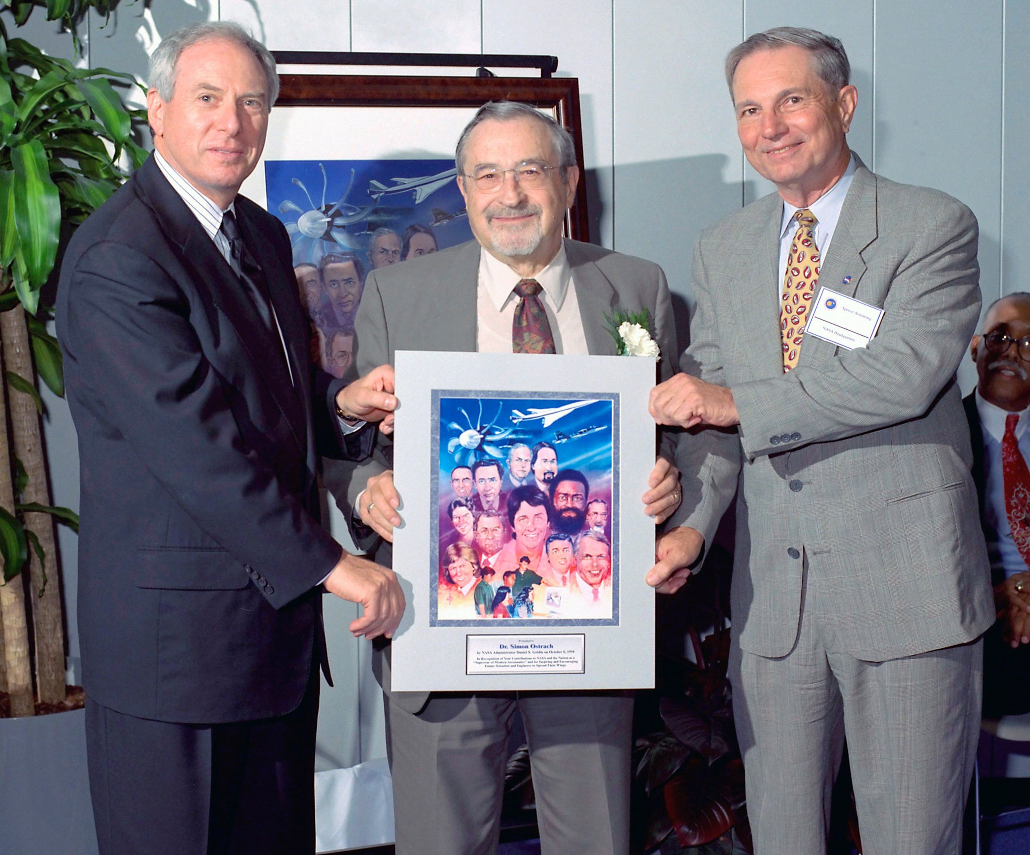 Three men standing, one holding poster.