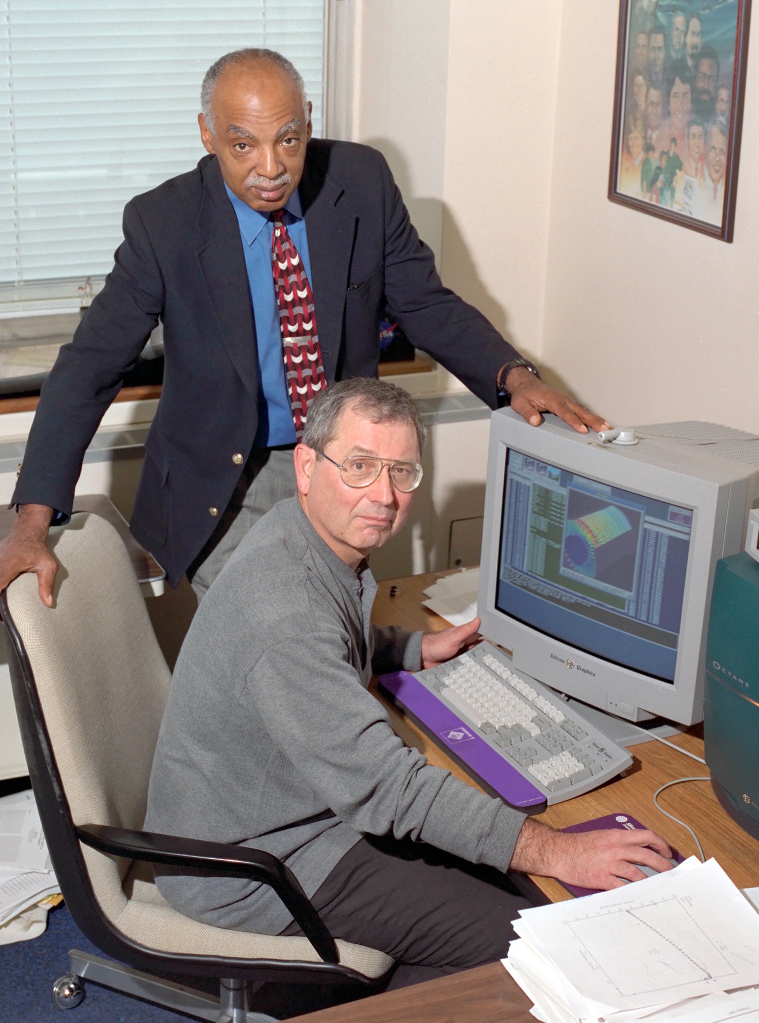 Man at computer screen and man standing.