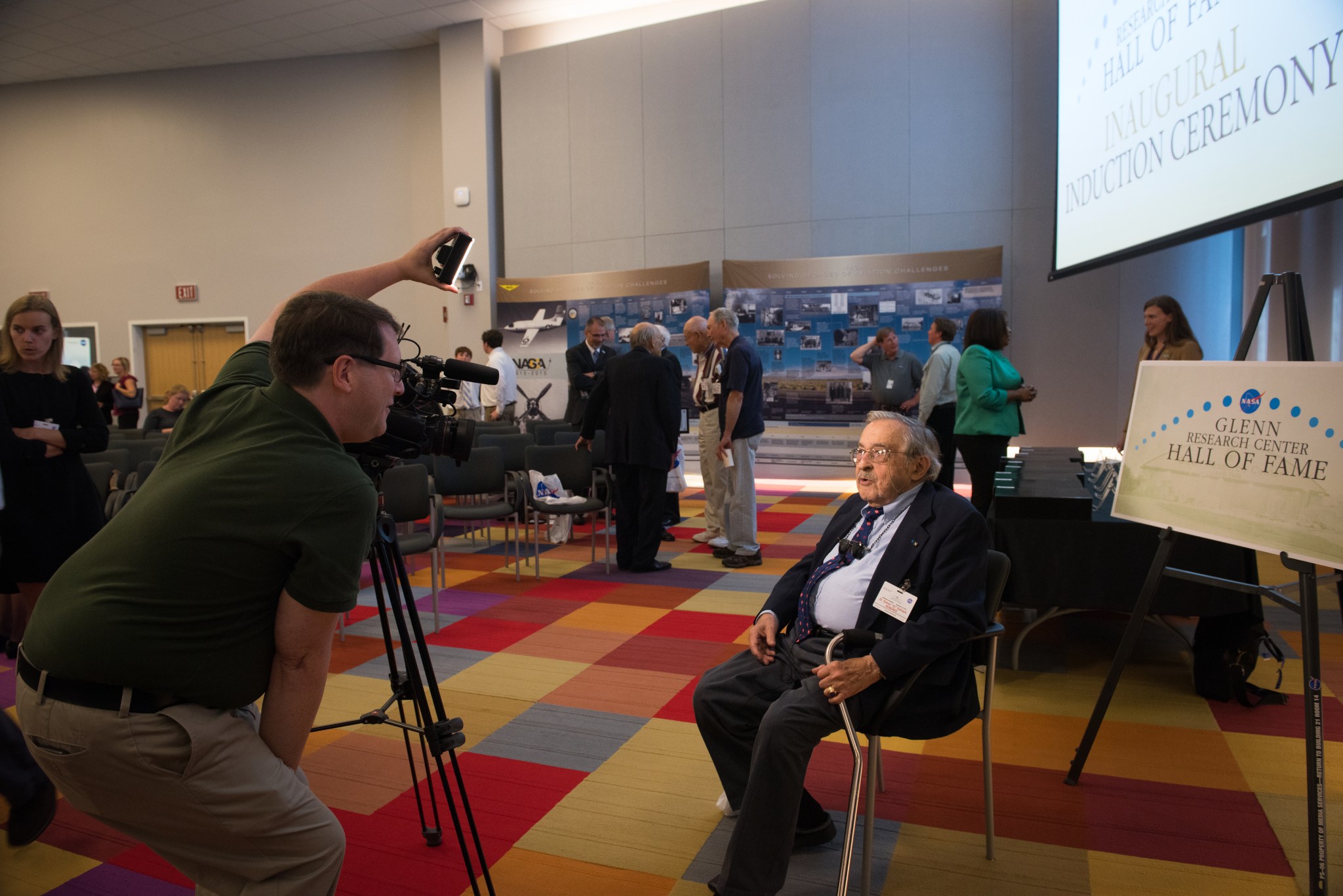 Man seated in front of video camera and photographer.