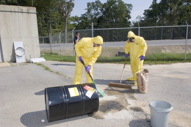 Two people in hazardous material suits cleanup a spill.