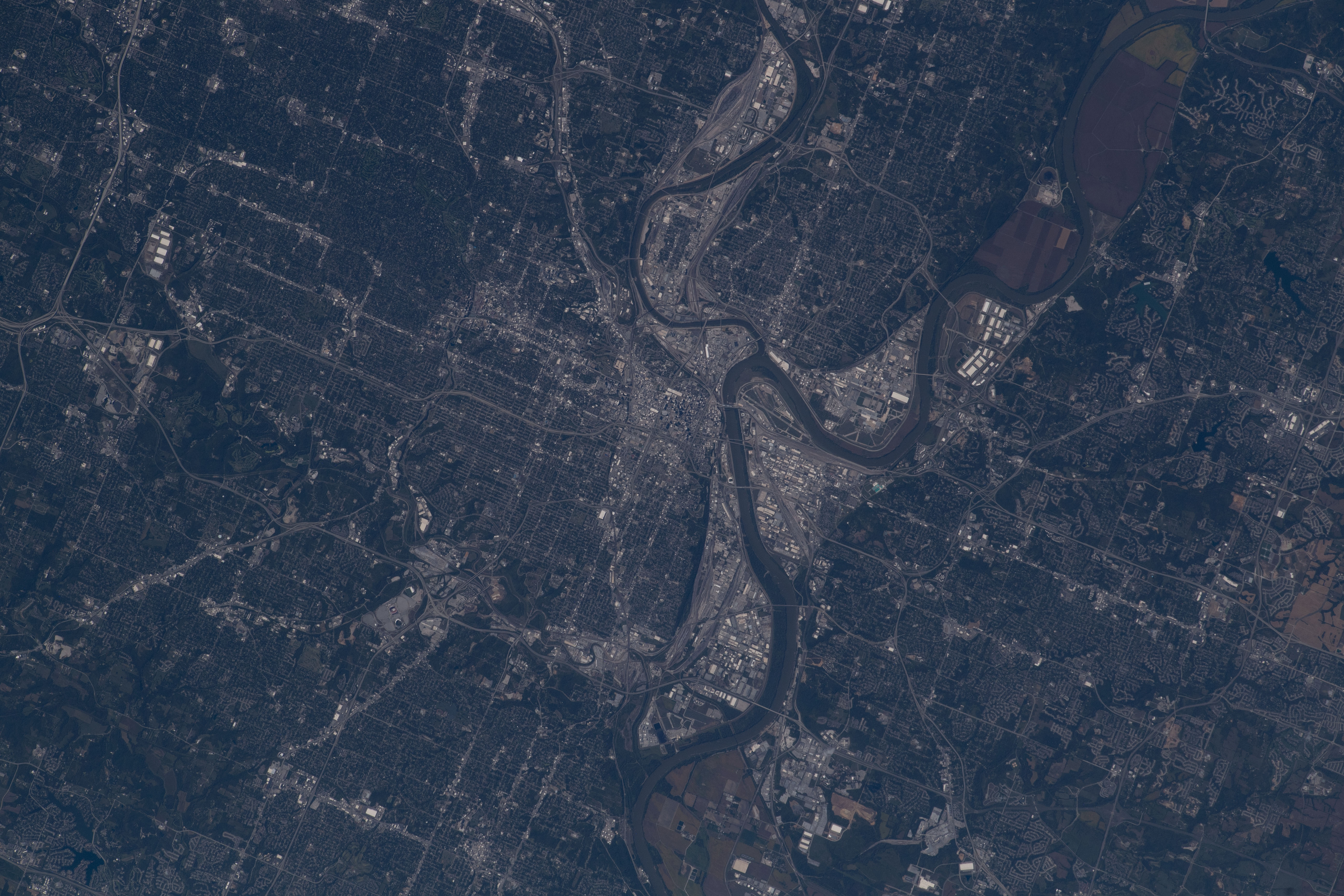 A view of Kansas City, Missouri, from space. The winding Missouri River is the focal point of the image, and Arrowhead Stadium is visible to the lower left of the river. The land is green, while the downtown city areas appear gray.