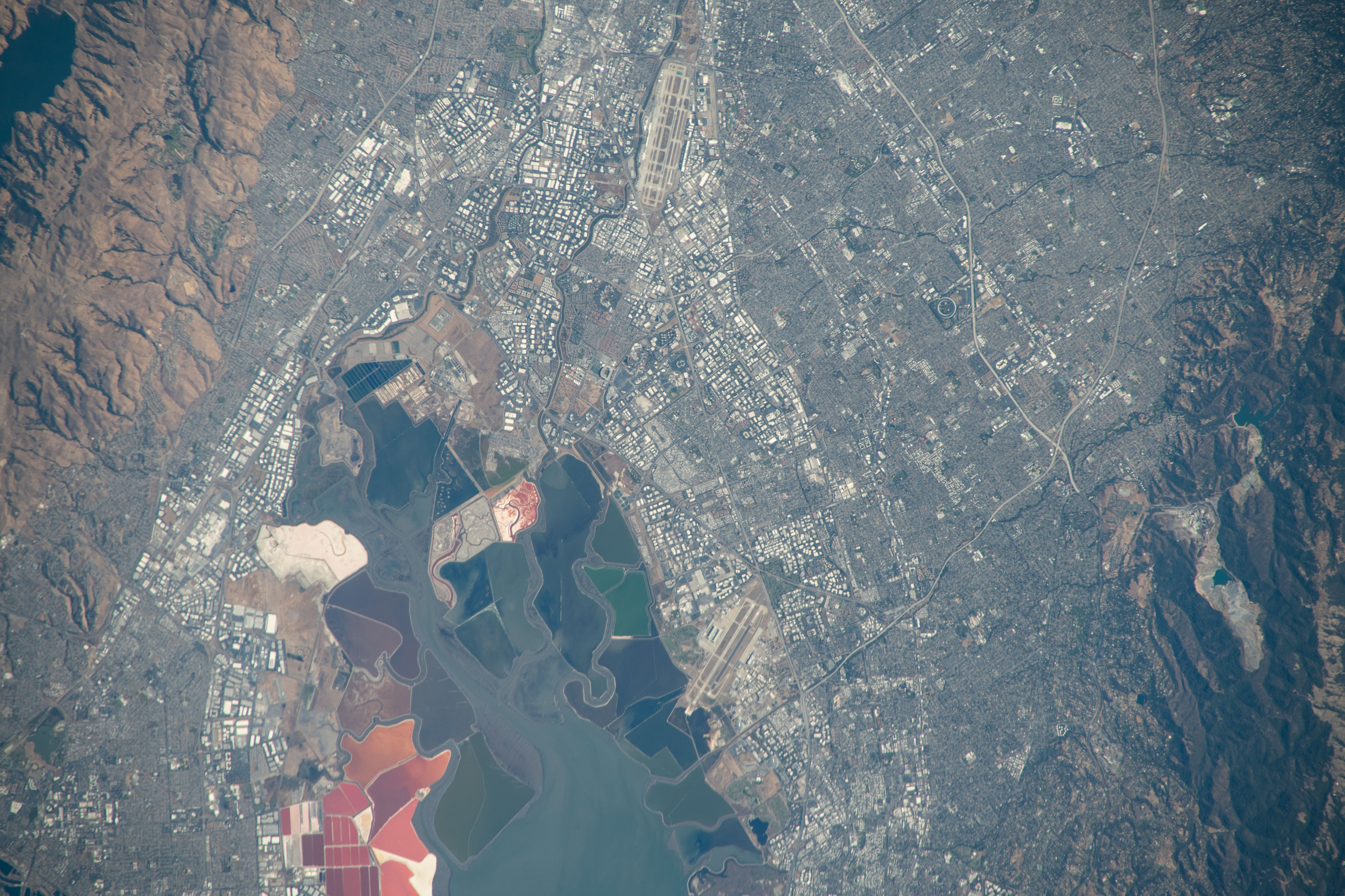 A view of Santa Clara, California, from space. San Francisco Bay is the focal point of the image, and Levi's Stadium is visible just above the bay near the center of the image. The land is a mixture of reds and greens, the mountains are brown, the water is a mixture of blues and greens, and the city areas appear gray.