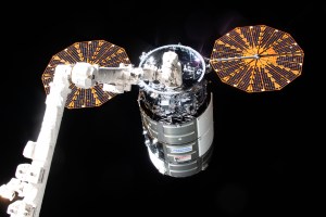 Northrop Grumman's Cygnus space freighter, packed with more than 8,200 pounds of science experiments, crew supplies, and station hardware, is pictured in the grips of the Canadarm2 robotic arm after its capture. Featured prominently on Cygnus, are its two cymbal-shaped UltraFlex solar arrays.